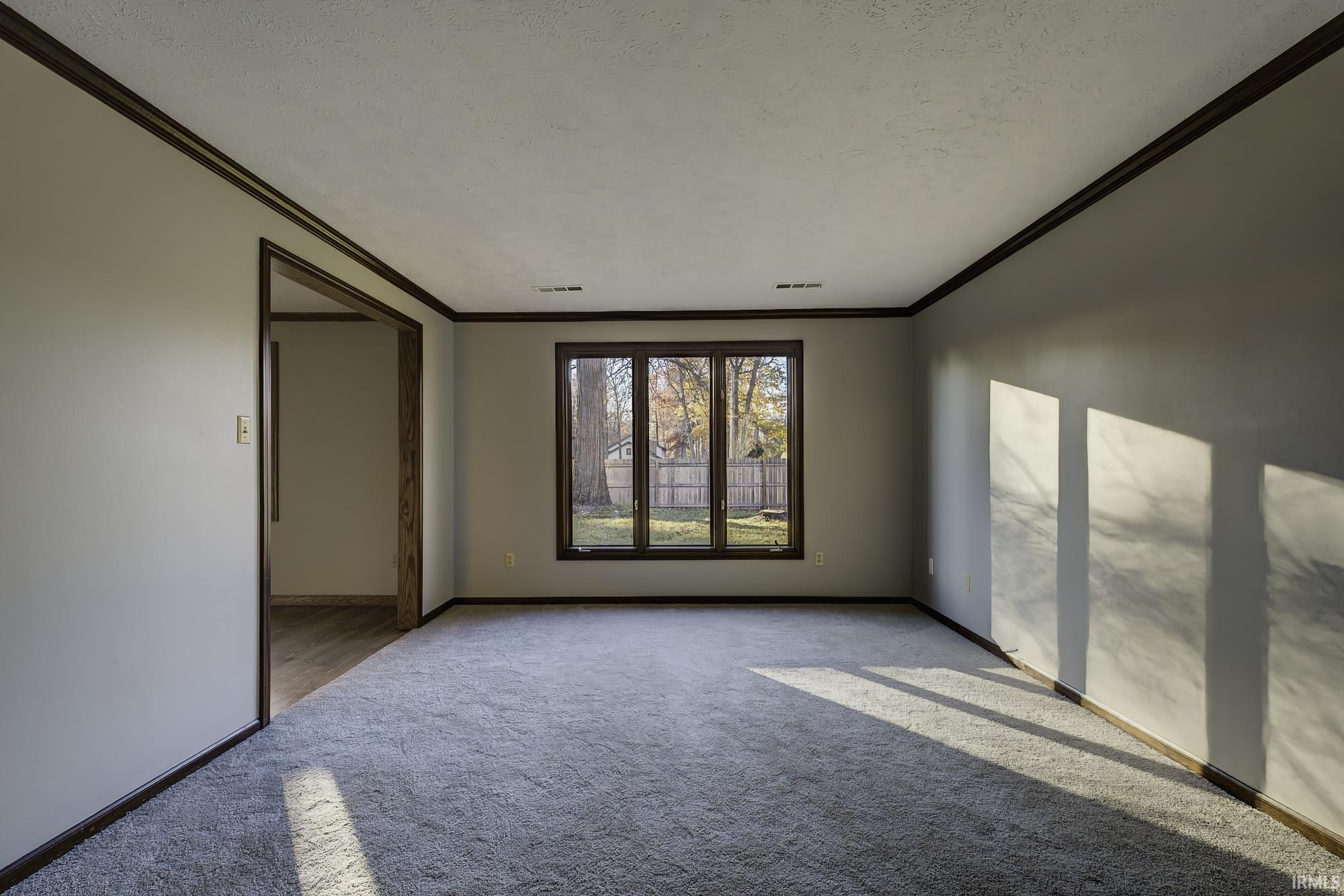 Empty room with ornamental molding, carpet flooring, and a textured ceiling