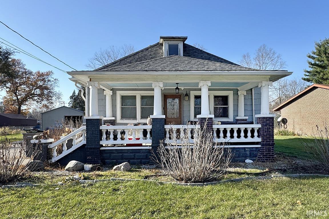 View of front of home featuring covered porch, roof with shingles, and a front yard