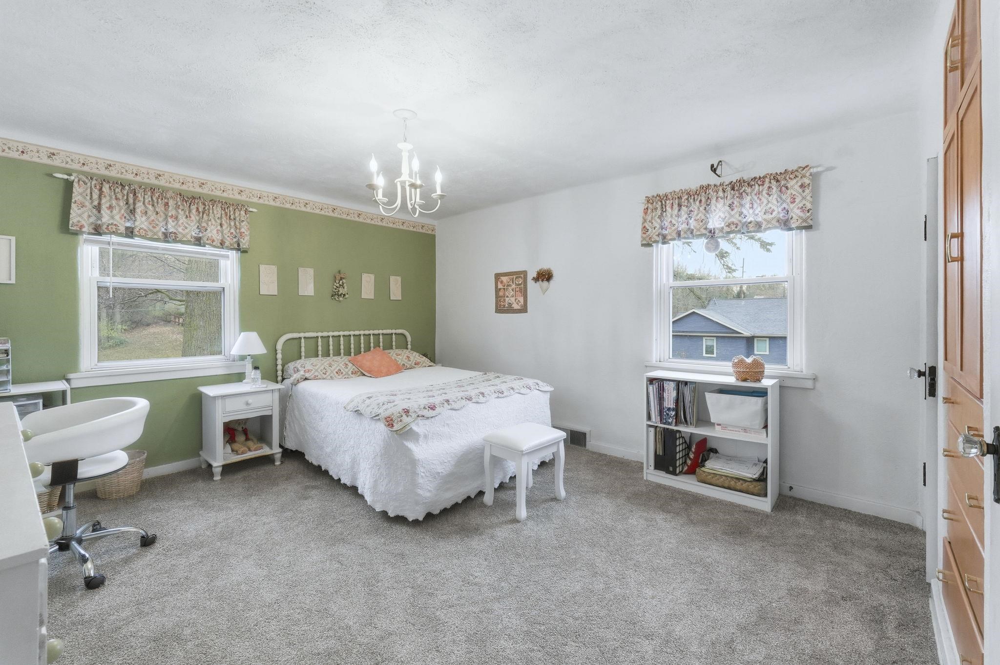 Bedroom with light carpet, multiple windows, and a chandelier