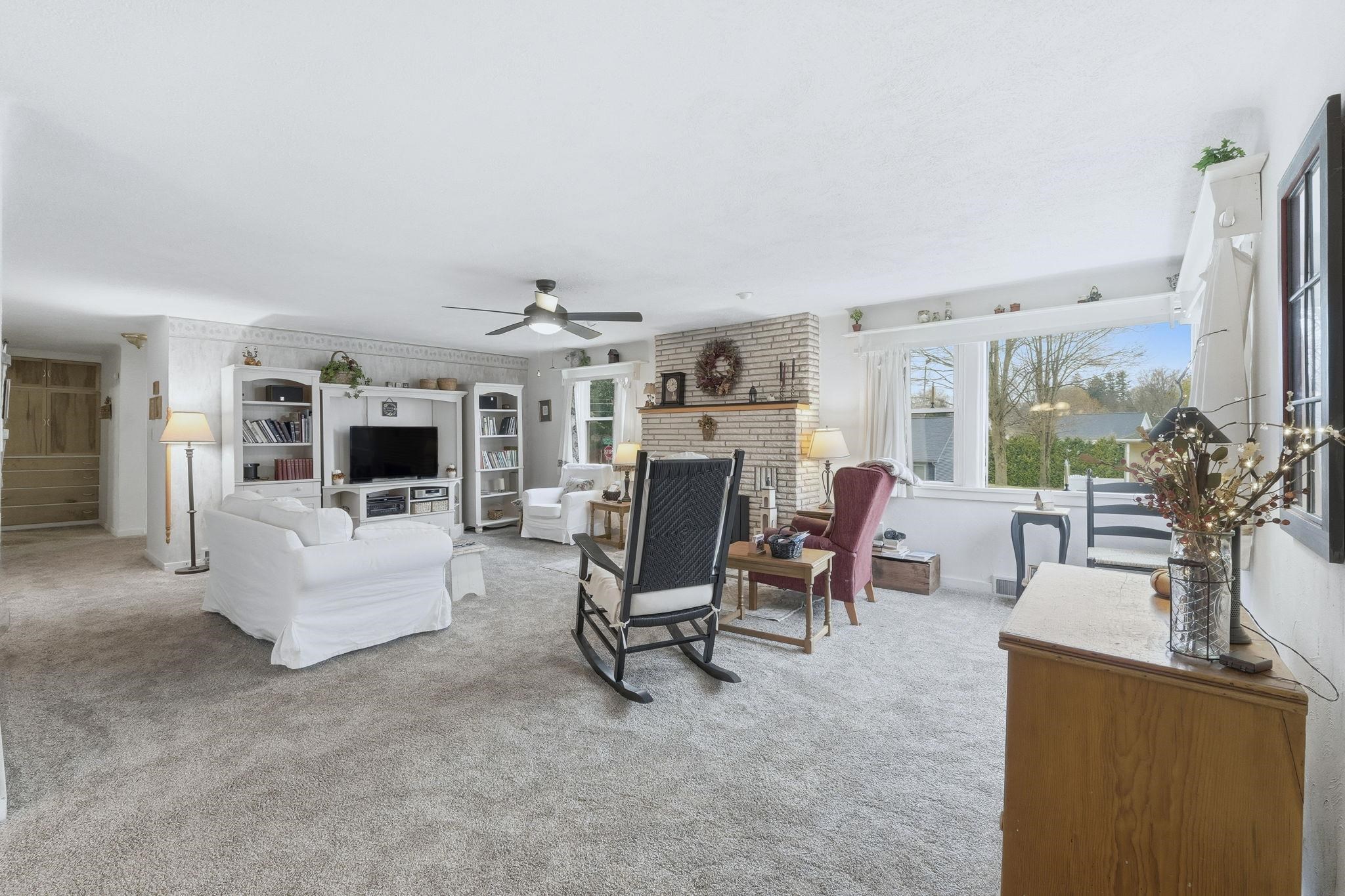 Living room with light carpet, a fireplace, and a ceiling fan