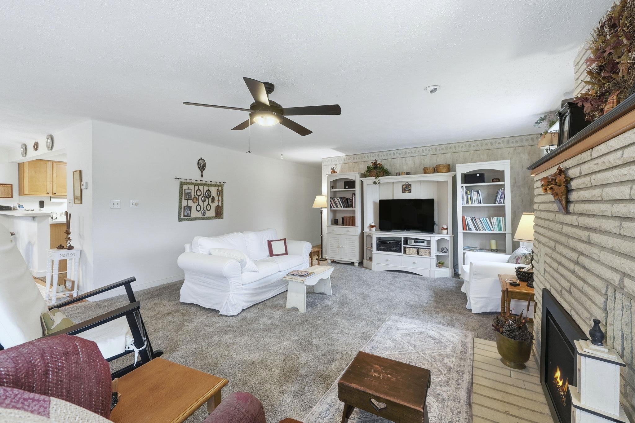 Living area with a brick fireplace, light colored carpet, and a ceiling fan