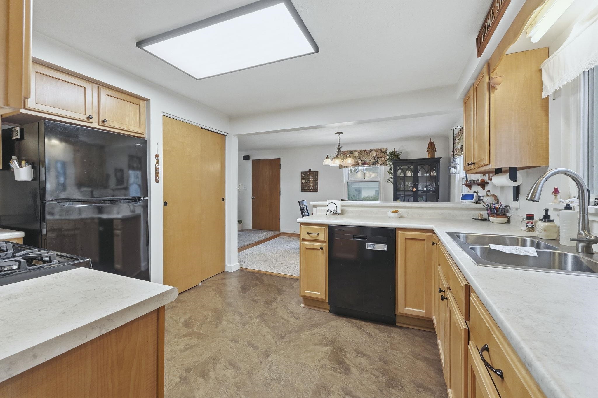 Kitchen featuring black appliances, light countertops, a peninsula, pendant lighting, and light brown cabinetry