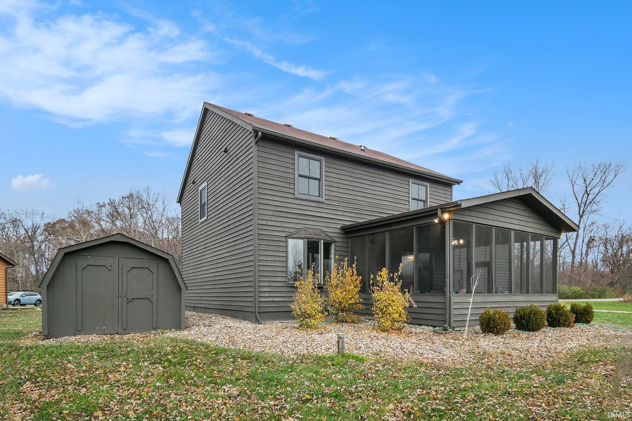 Rear view of property with a storage unit, a sunroom, and a yard