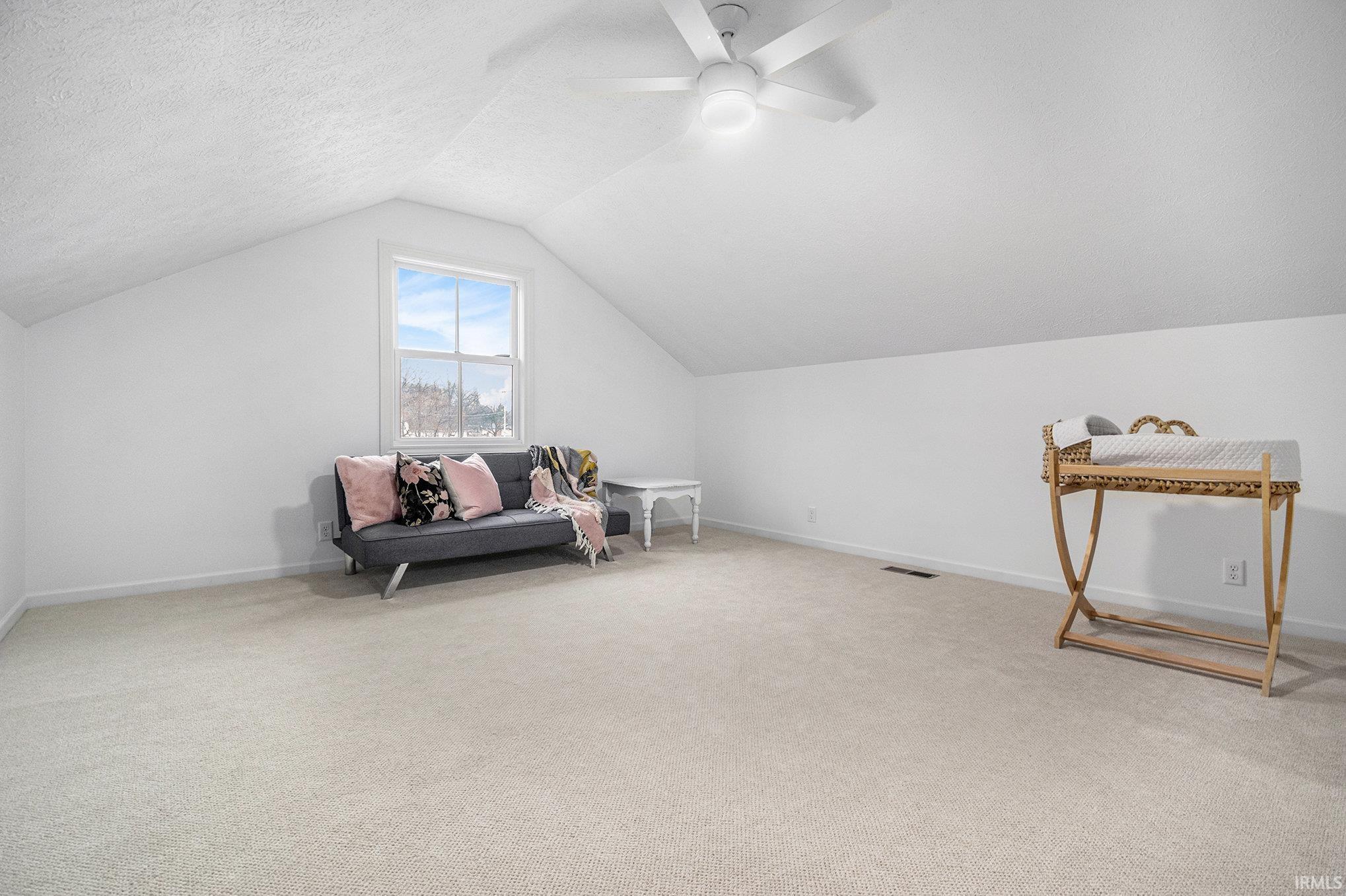 Living area with vaulted ceiling, light carpet, a textured ceiling, and ceiling fan