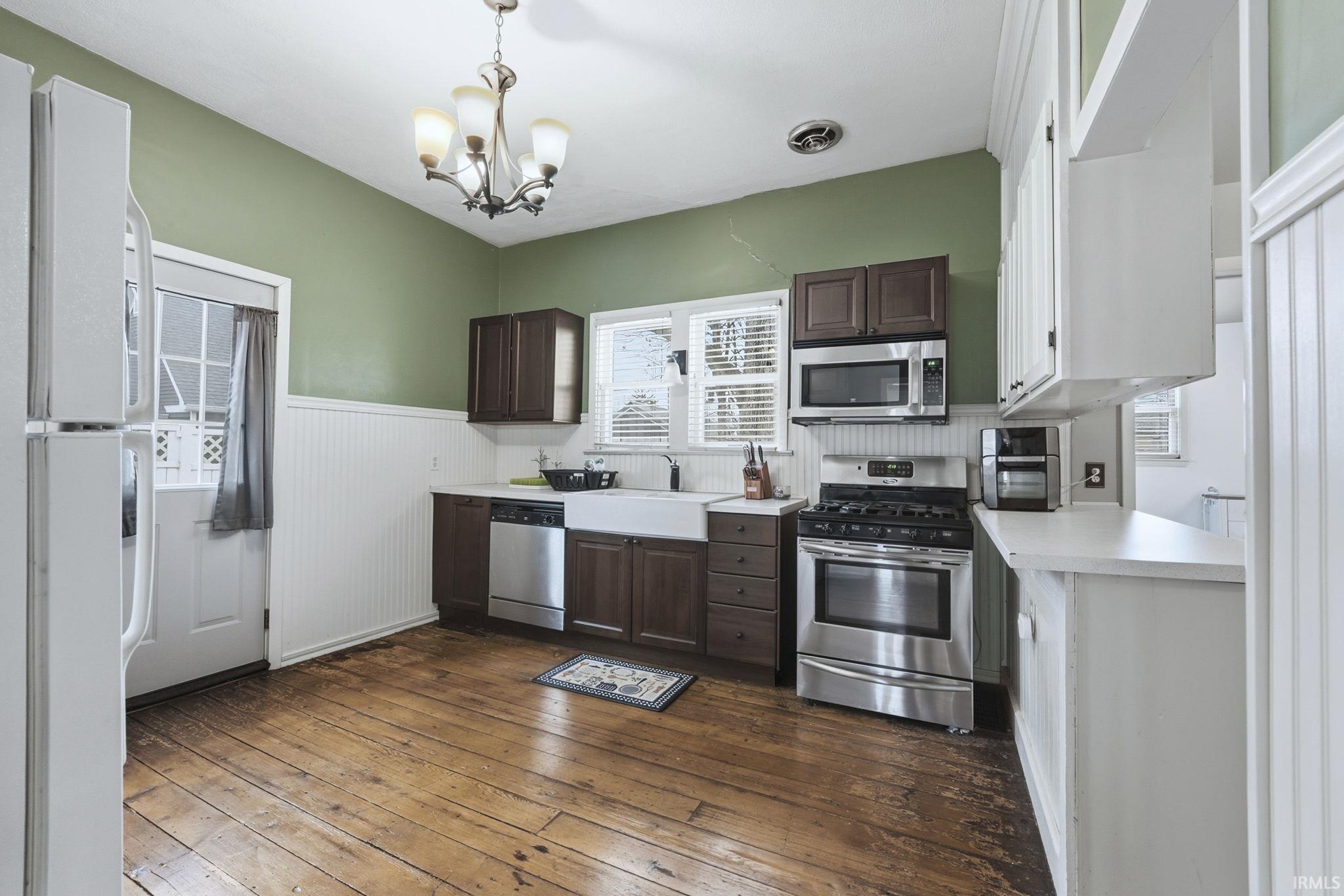 Kitchen with dark brown cabinets, light countertops, stainless steel appliances, dark wood-style flooring, and a wainscoted wall