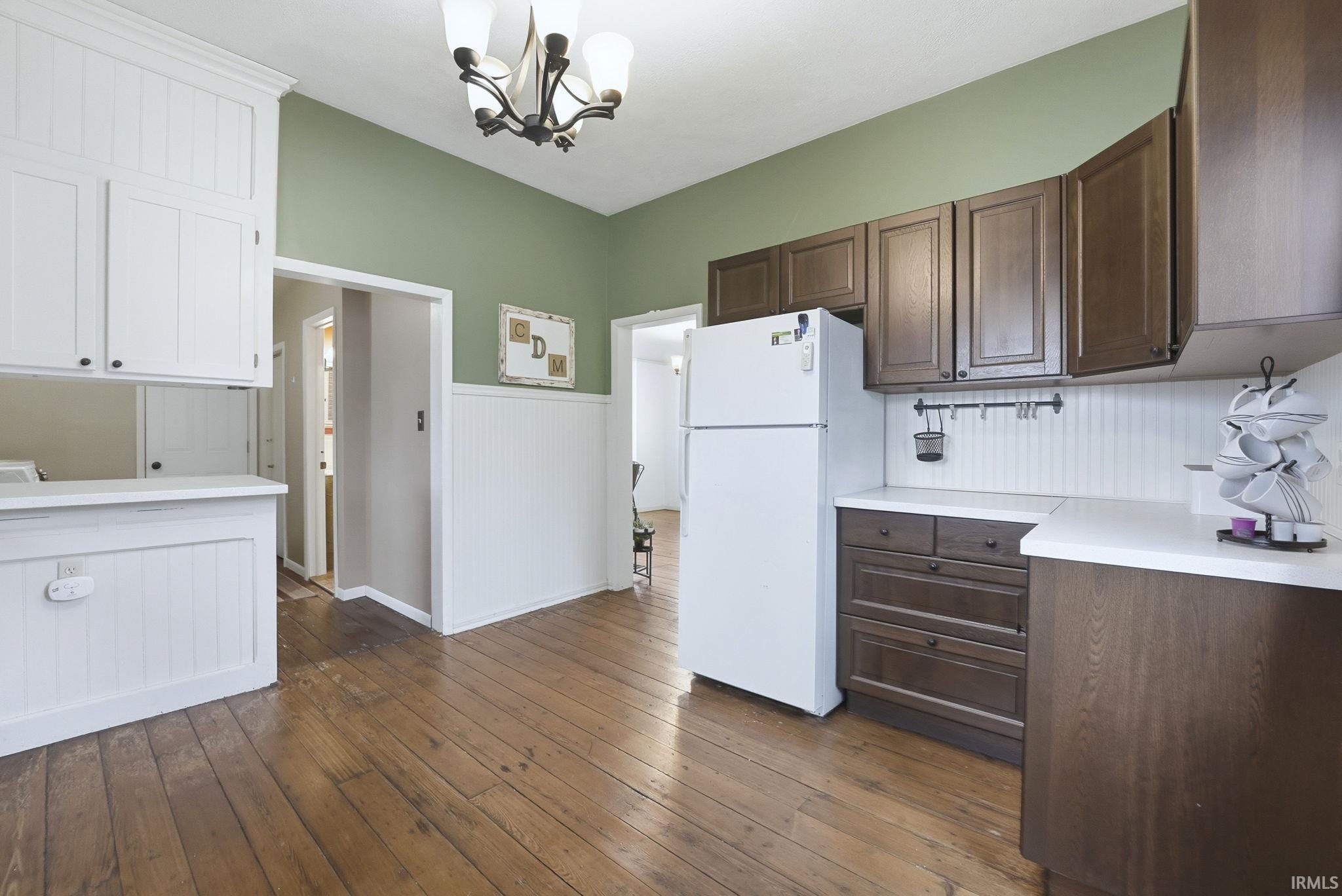 Kitchen with light countertops, freestanding refrigerator, dark wood-style flooring, a chandelier, and decorative light fixtures