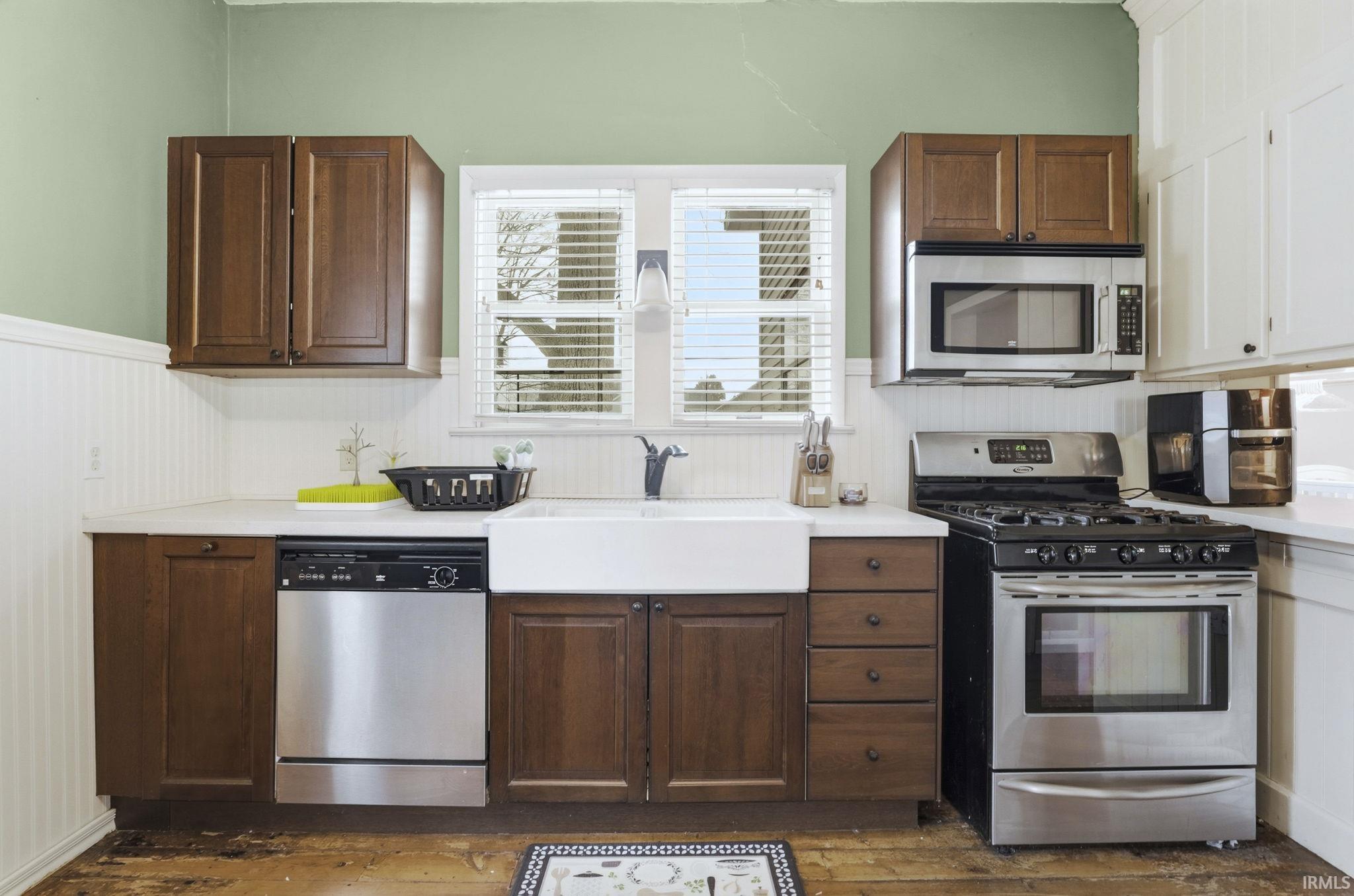 Kitchen with appliances with stainless steel finishes, light countertops, dark wood-type flooring, and wainscoting