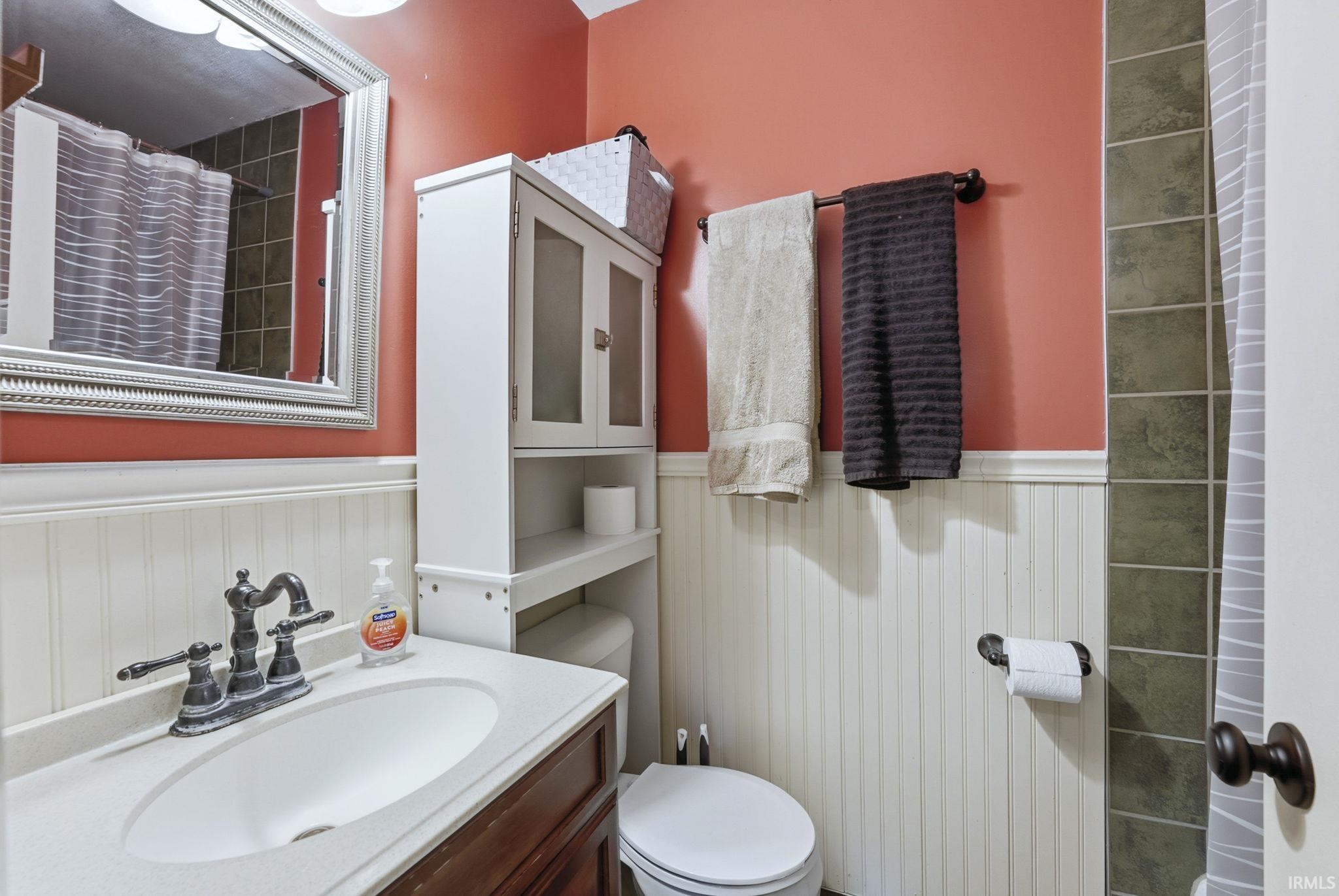 Bathroom with a shower with shower curtain, vanity, and a wainscoted wall