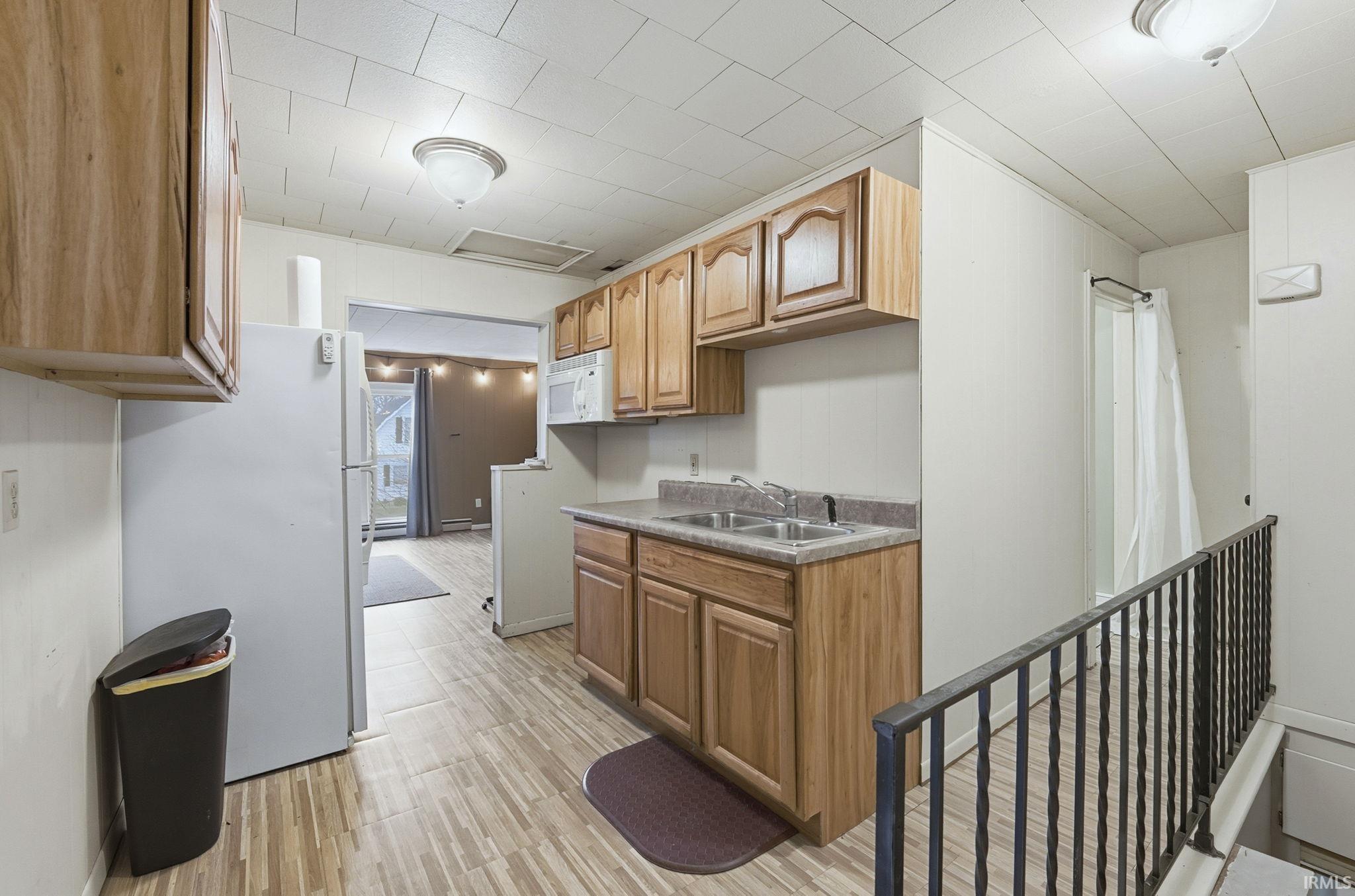 Kitchen featuring white appliances, light wood-style flooring, brown cabinetry, and light countertops