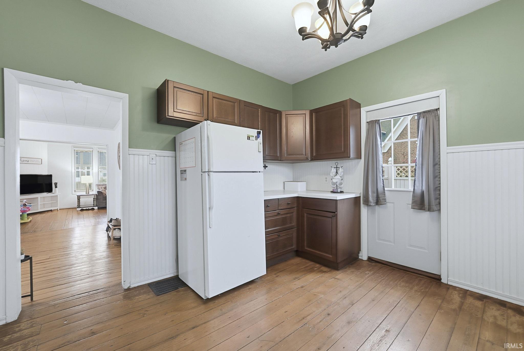 Kitchen with freestanding refrigerator, light countertops, light wood finished floors, a chandelier, and wainscoting