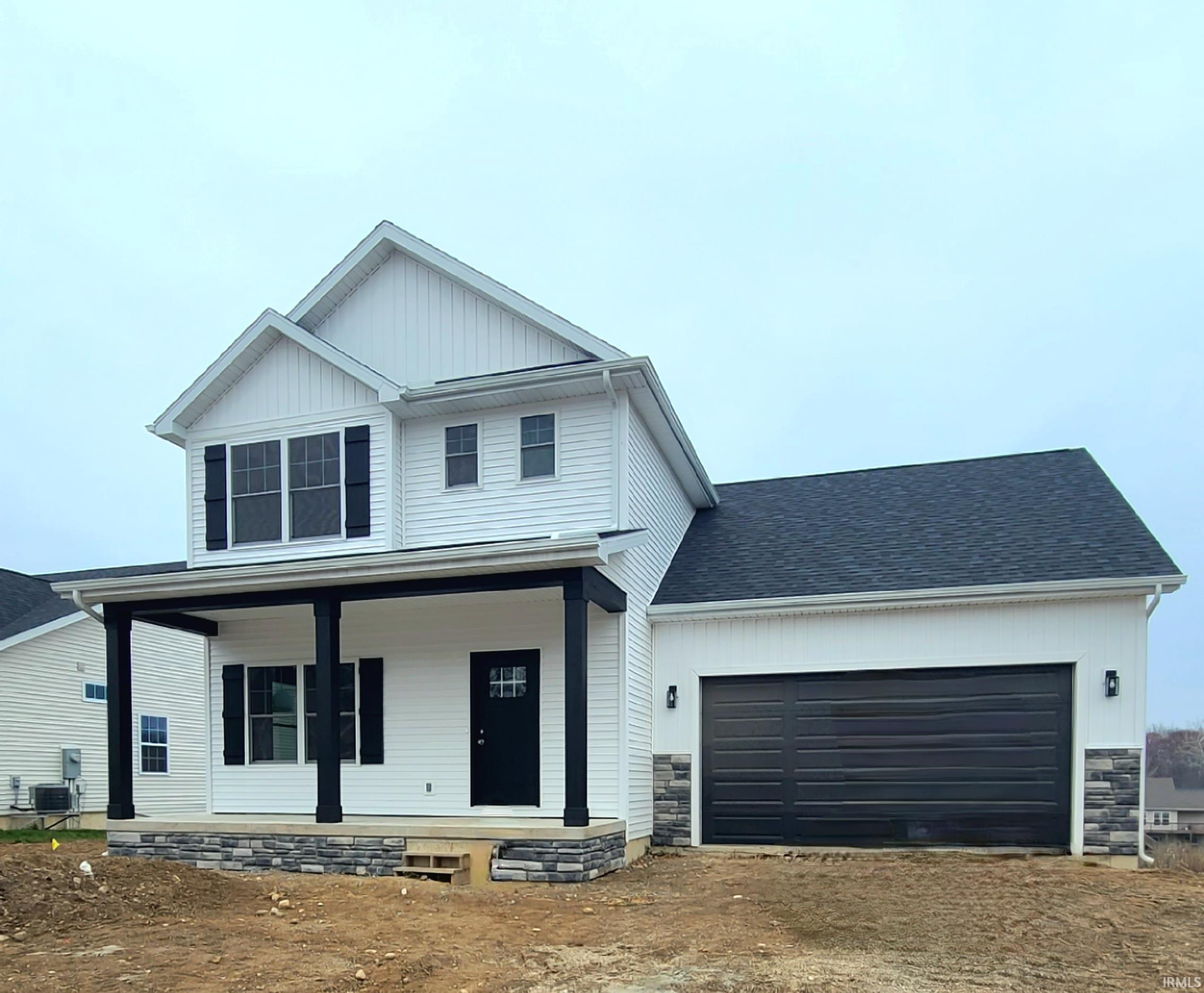 View of front facade featuring a porch, stone siding, dirt driveway, and a garage
