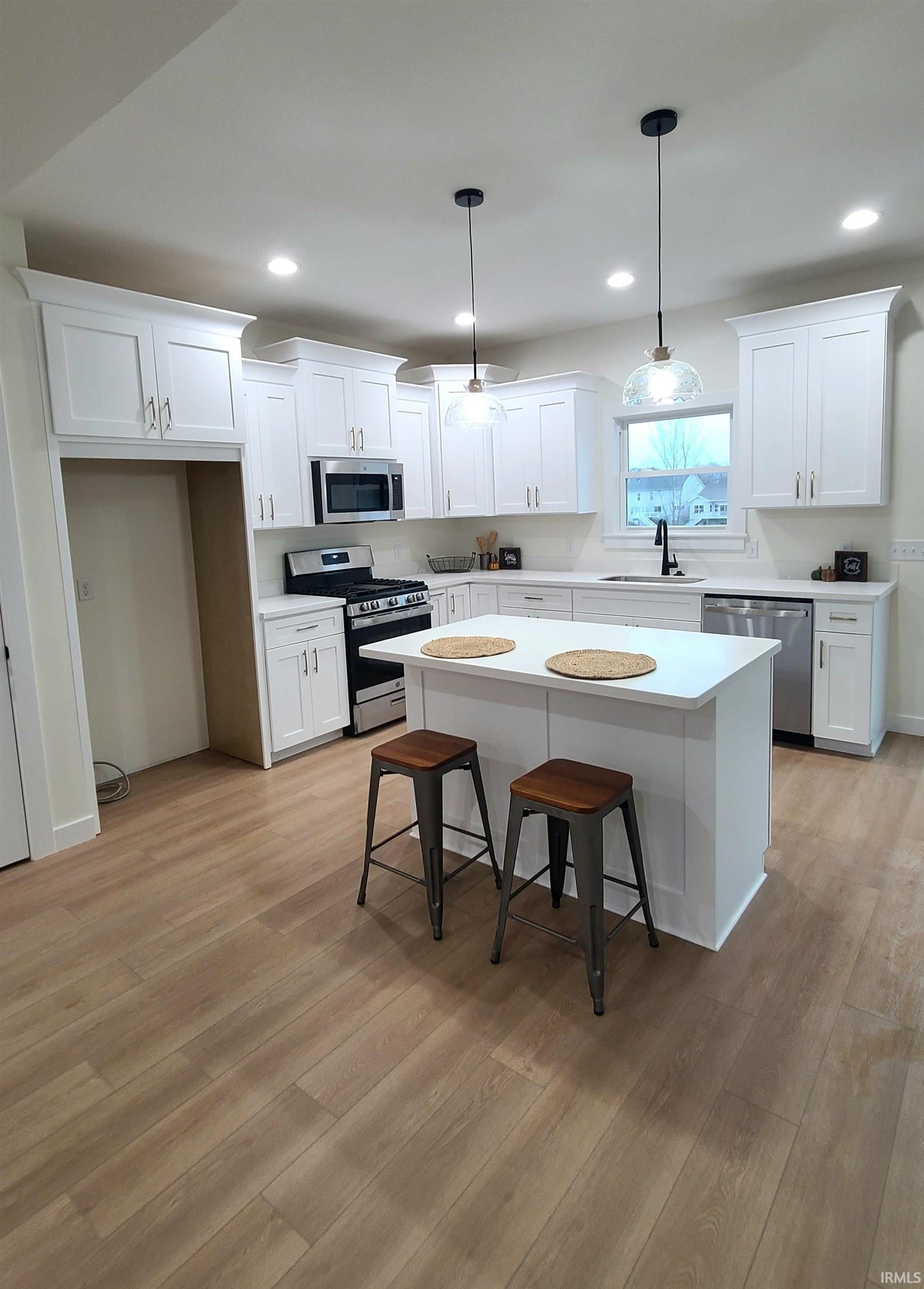Kitchen with a kitchen bar, stainless steel appliances, a center island, decorative light fixtures, and white cabinetry