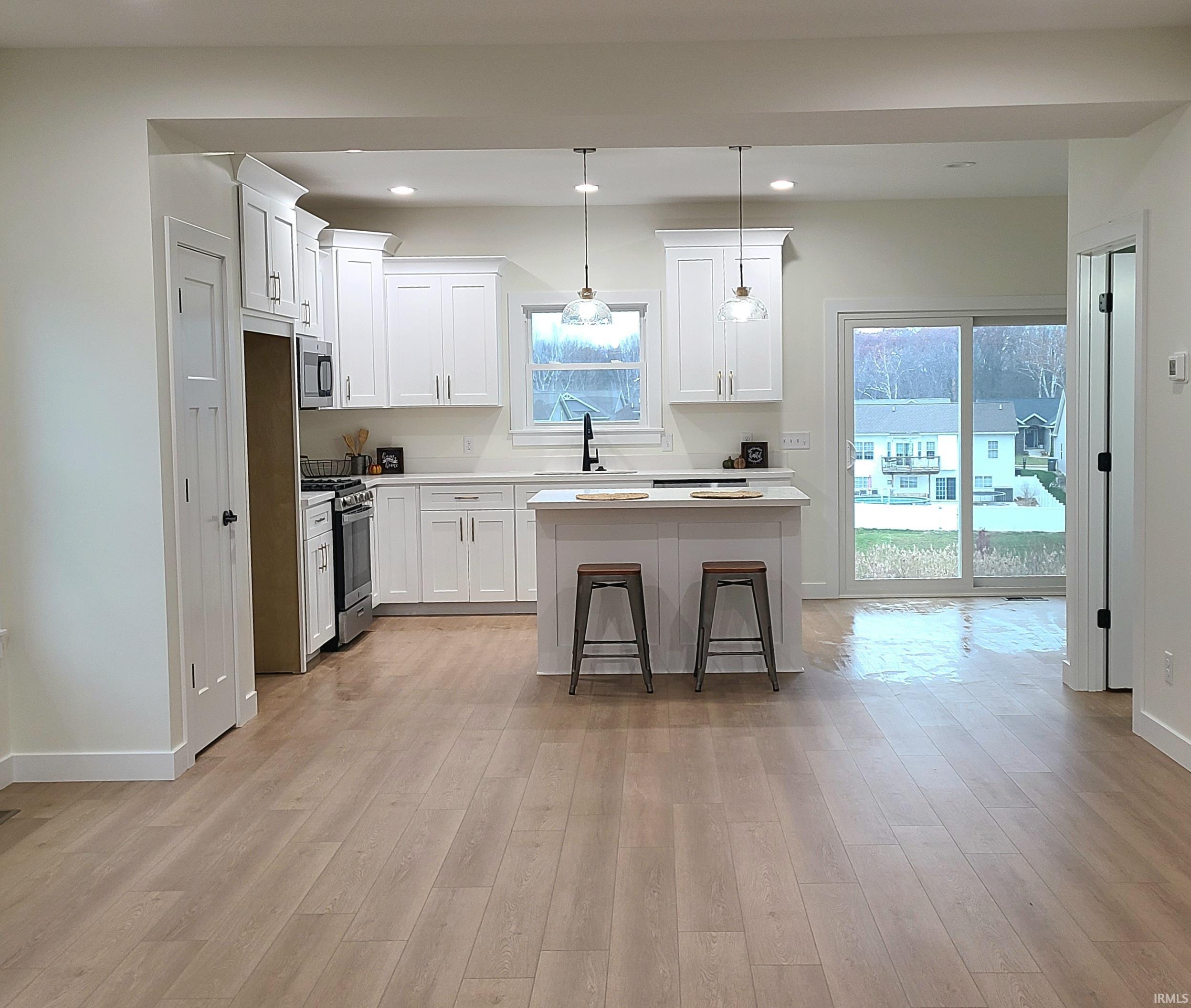 Kitchen with pendant lighting, a breakfast bar area, white cabinetry, stainless steel appliances, and a kitchen island