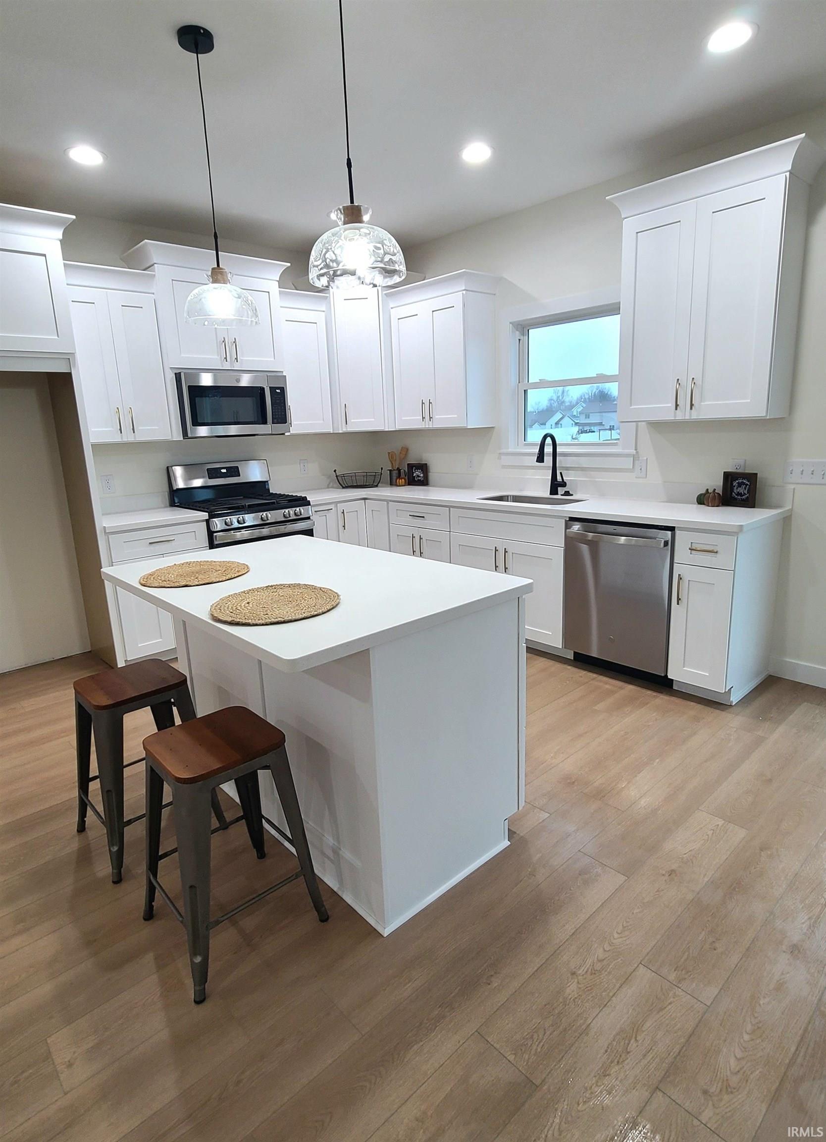 Kitchen with a breakfast bar area, white cabinets, appliances with stainless steel finishes, a center island, and recessed lighting