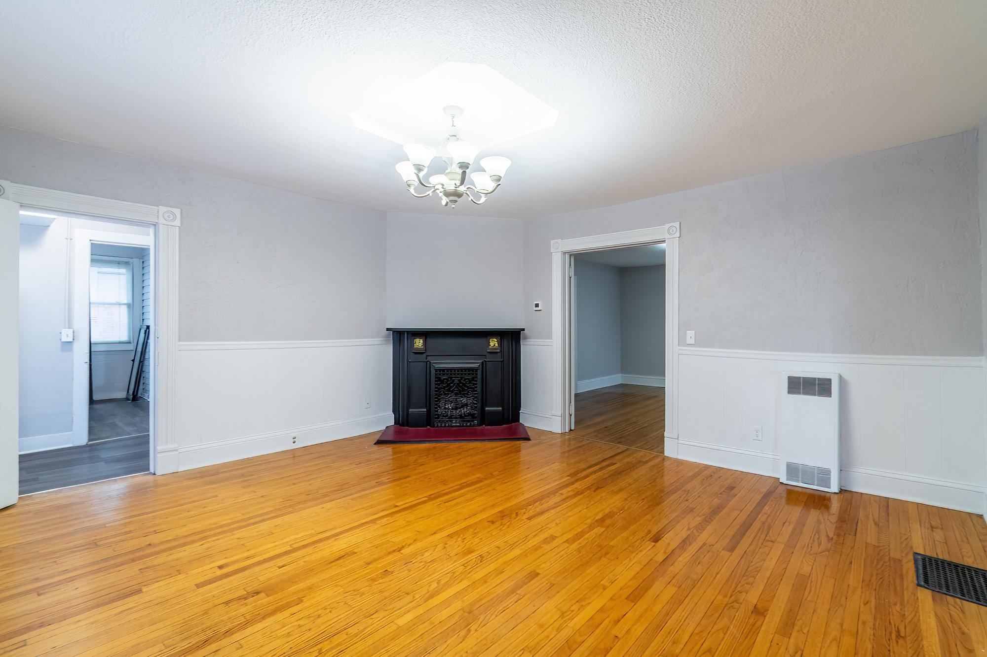 Unfurnished living room with hardwood / wood-style flooring, a fireplace with raised hearth, a chandelier, wainscoting, and a textured ceiling