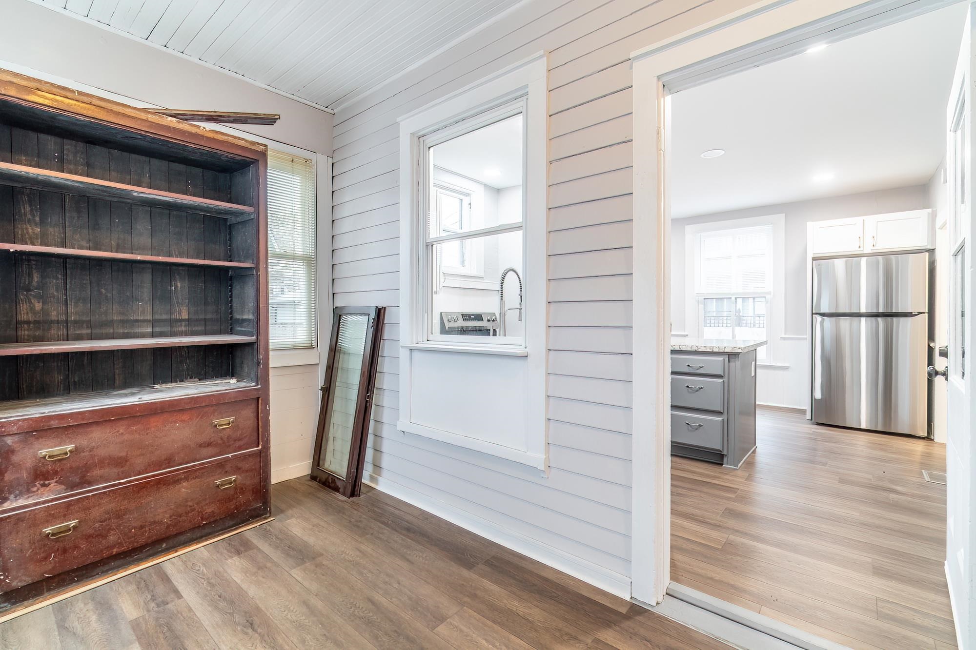 Kitchen view of light wood finished floors, freestanding refrigerator, gray cabinetry, open shelves, and wooden walls