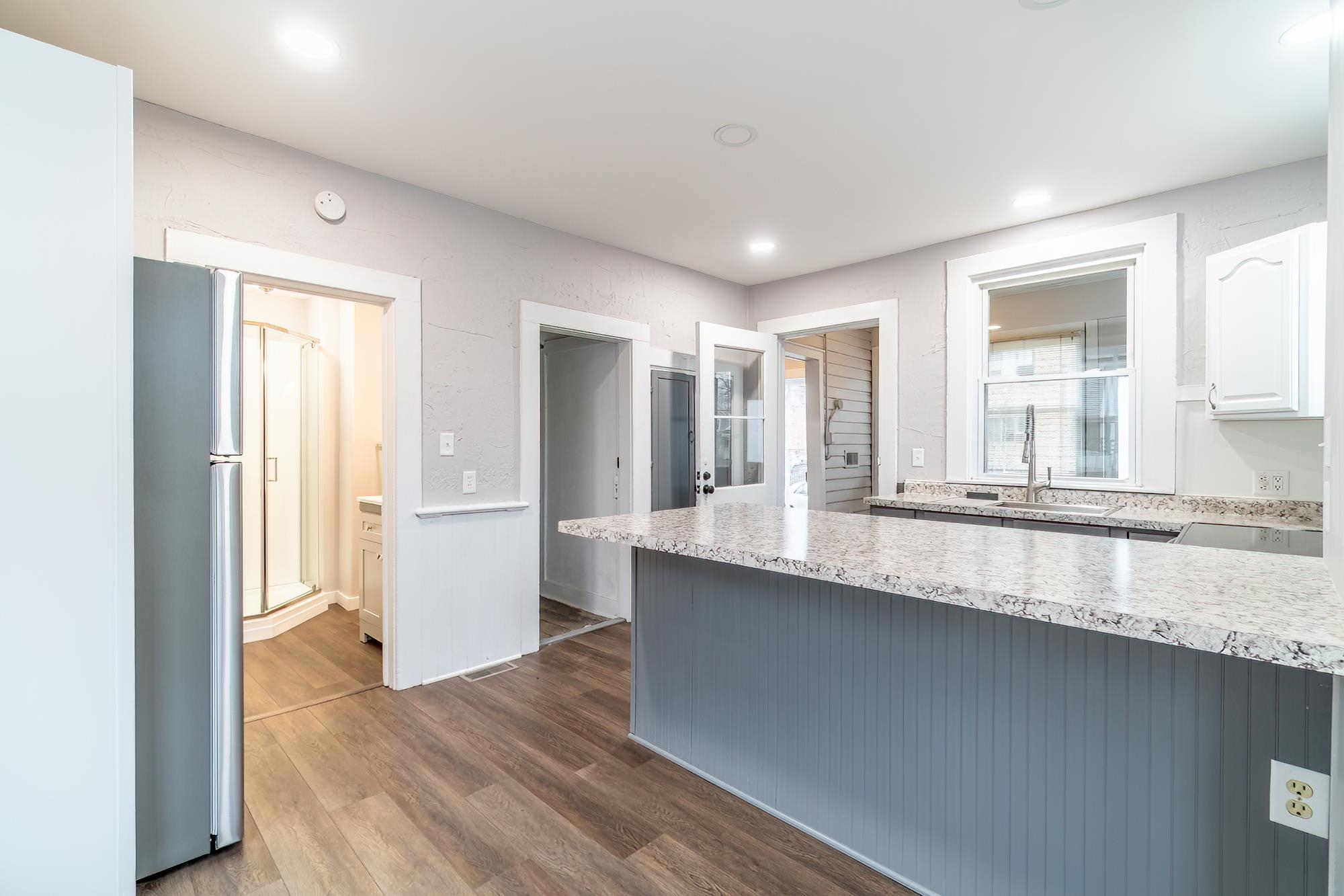 Kitchen with freestanding refrigerator, dark wood-style floors, white cabinets, light stone countertops, and a peninsula