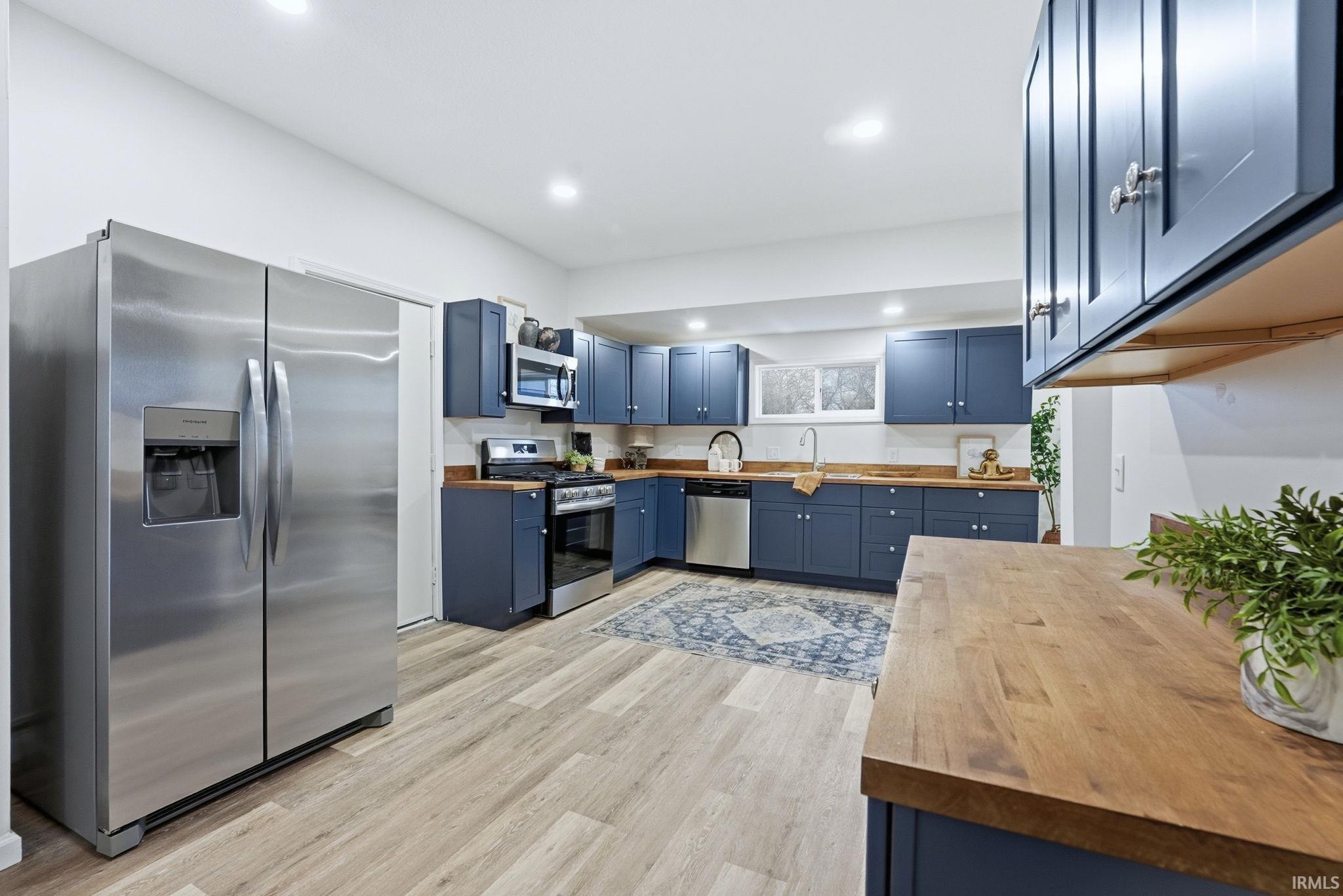 Kitchen featuring blue cabinetry, butcher block countertops, stainless steel appliances, light wood-type flooring, and recessed lighting