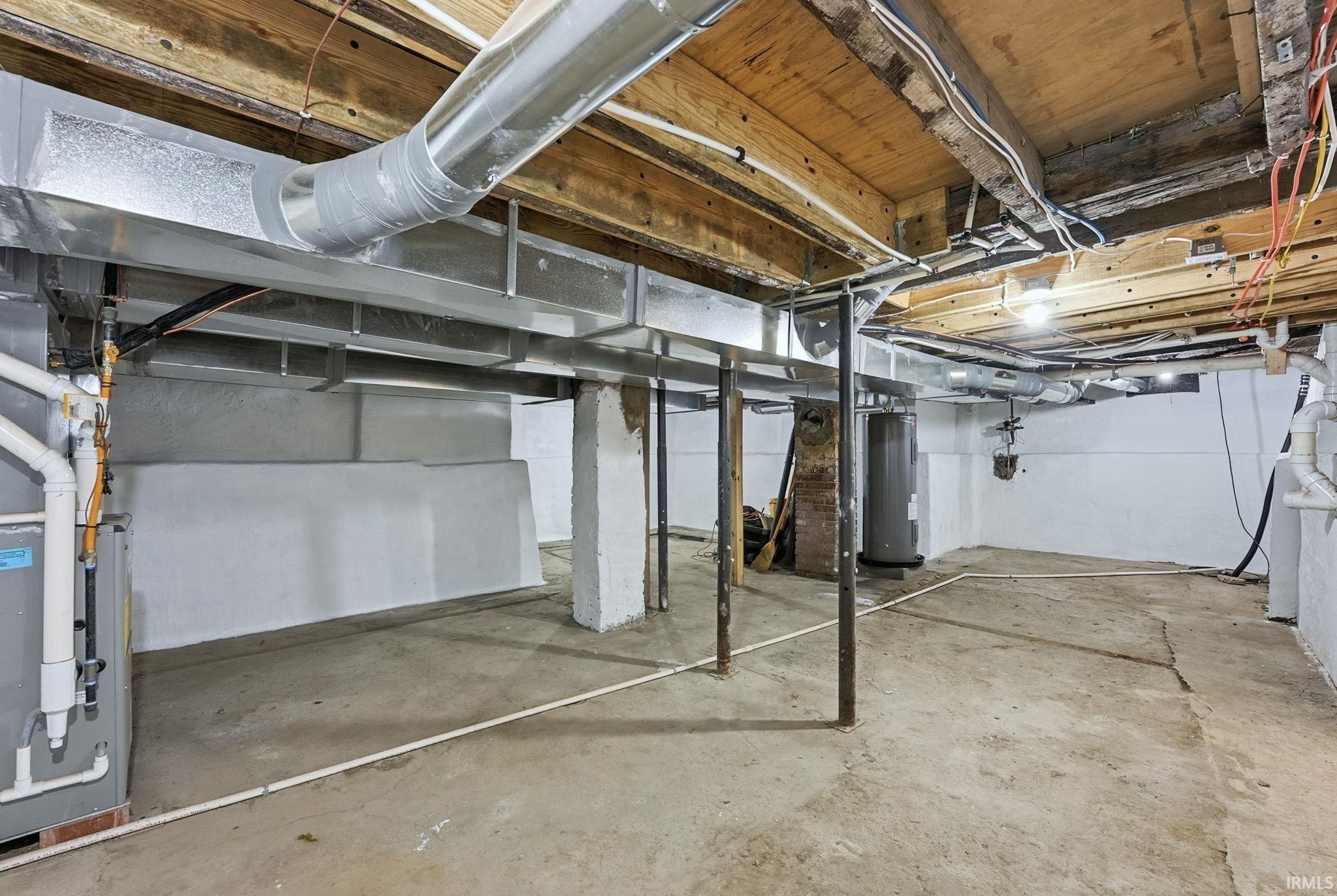 Unfinished below grade area featuring electric water heater and heating unit