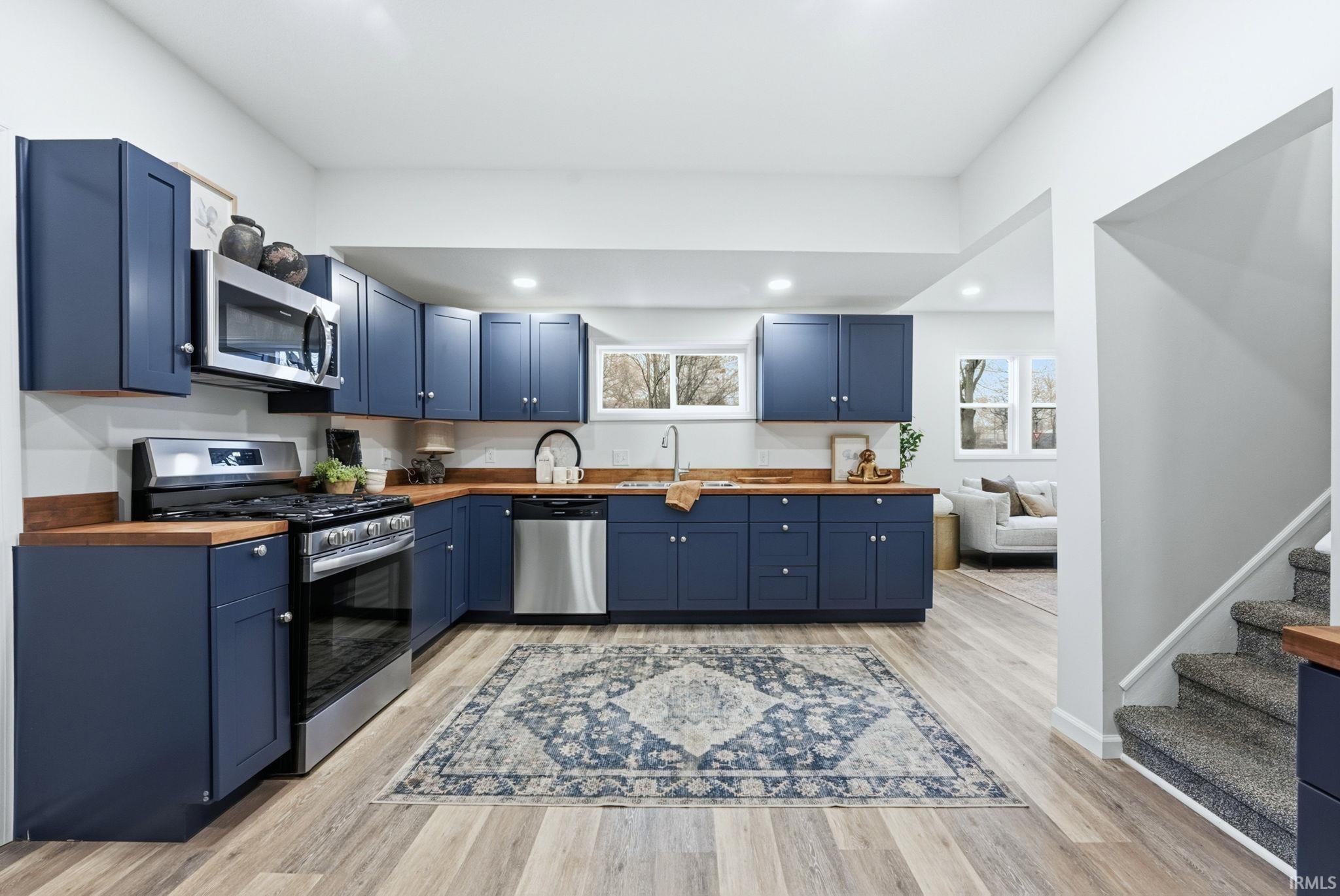 Kitchen with blue cabinetry, wooden counters, appliances with stainless steel finishes, and recessed lighting