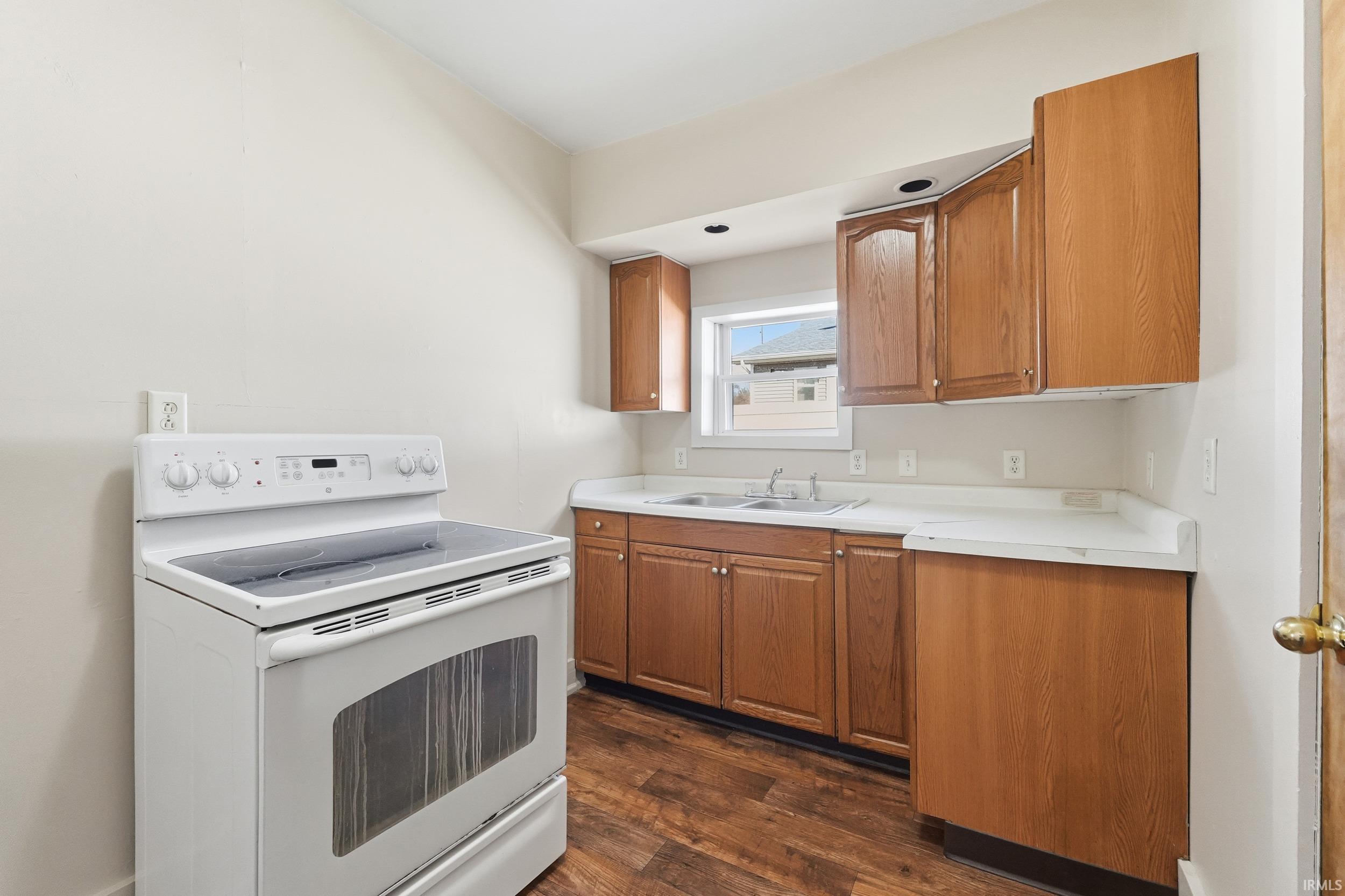Kitchen with electric range, dark wood finished floors, light countertops, and brown cabinets