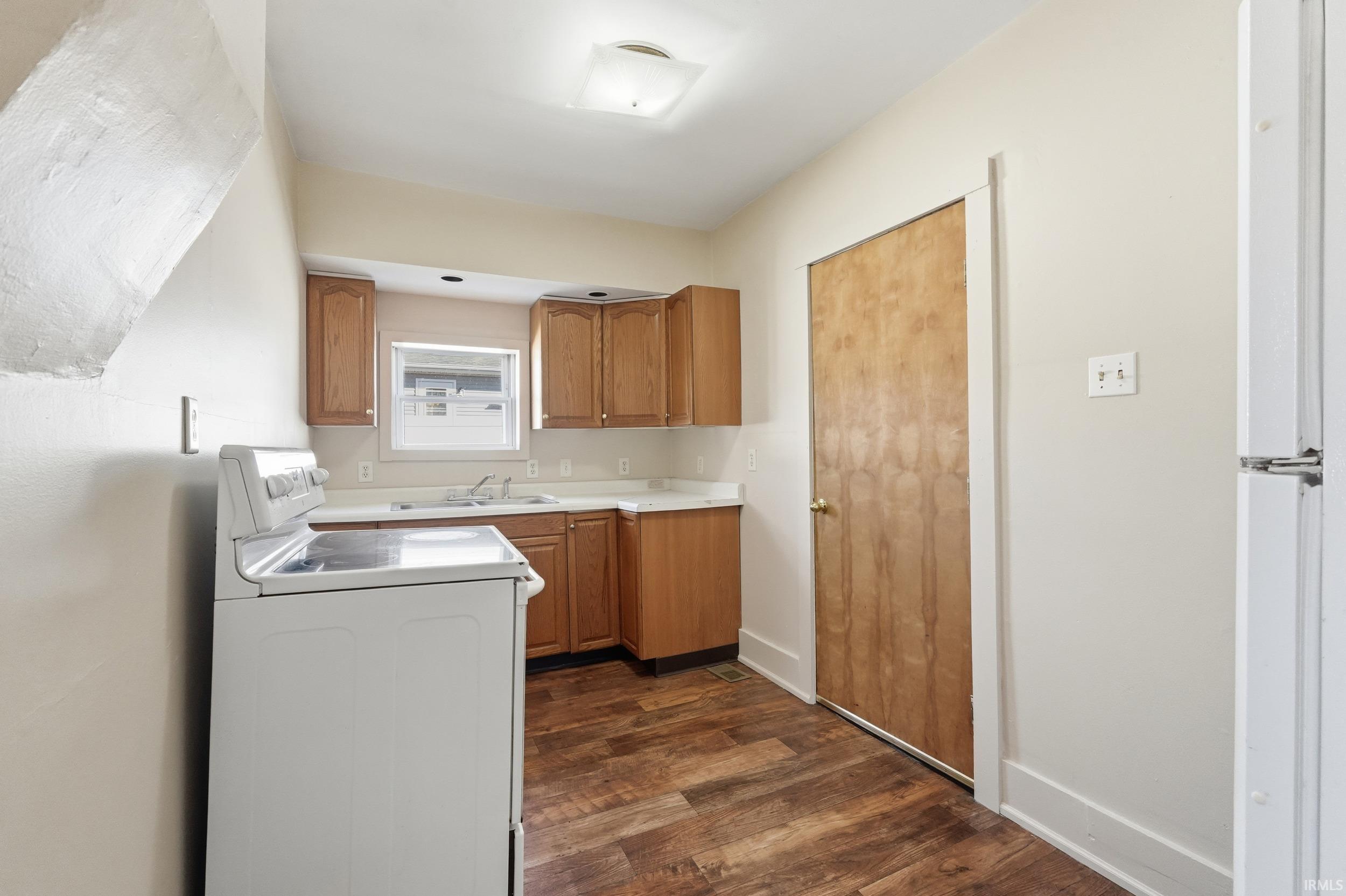 Kitchen with dark wood finished floors, light countertops, white appliances, brown cabinetry, and washer / clothes dryer