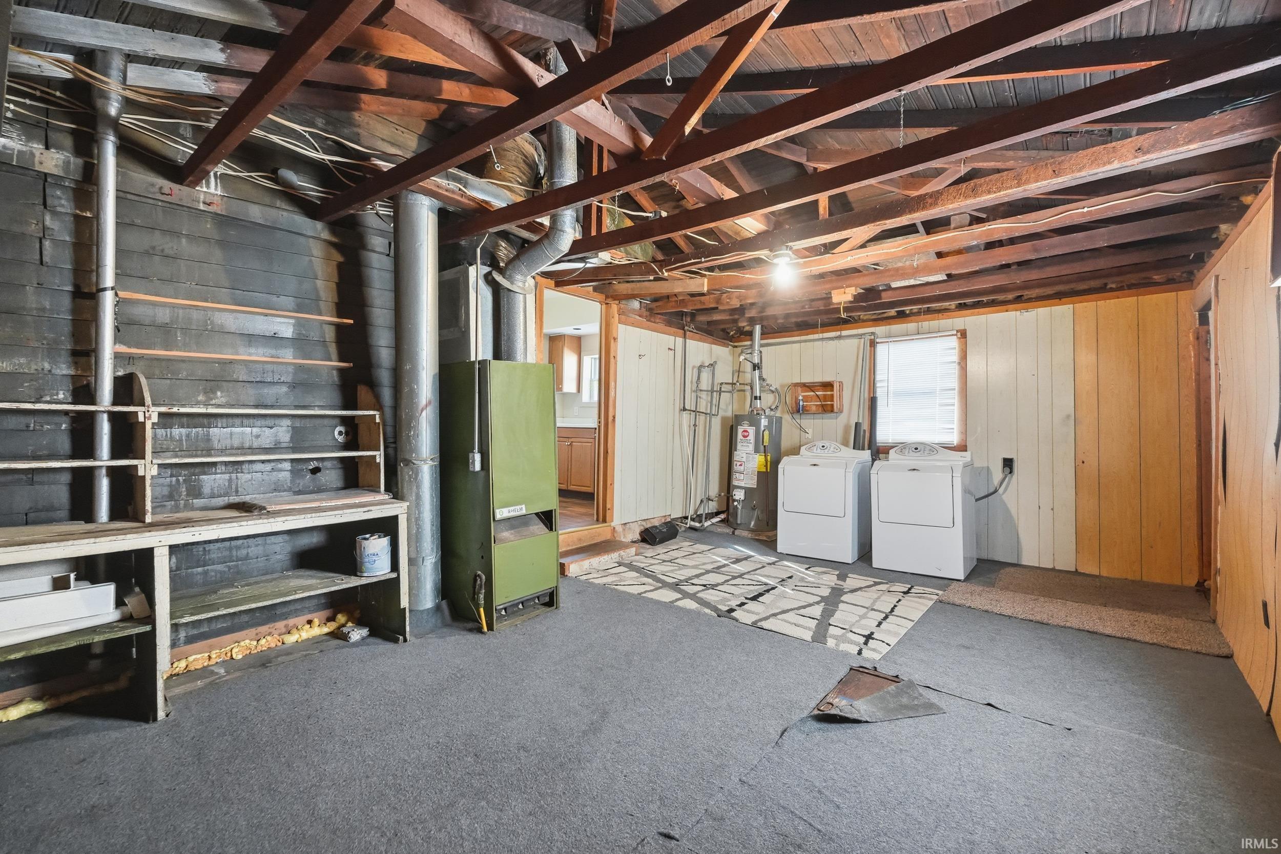 Below grade area with gas water heater, independent washer and dryer, wood walls, carpet, and heating unit