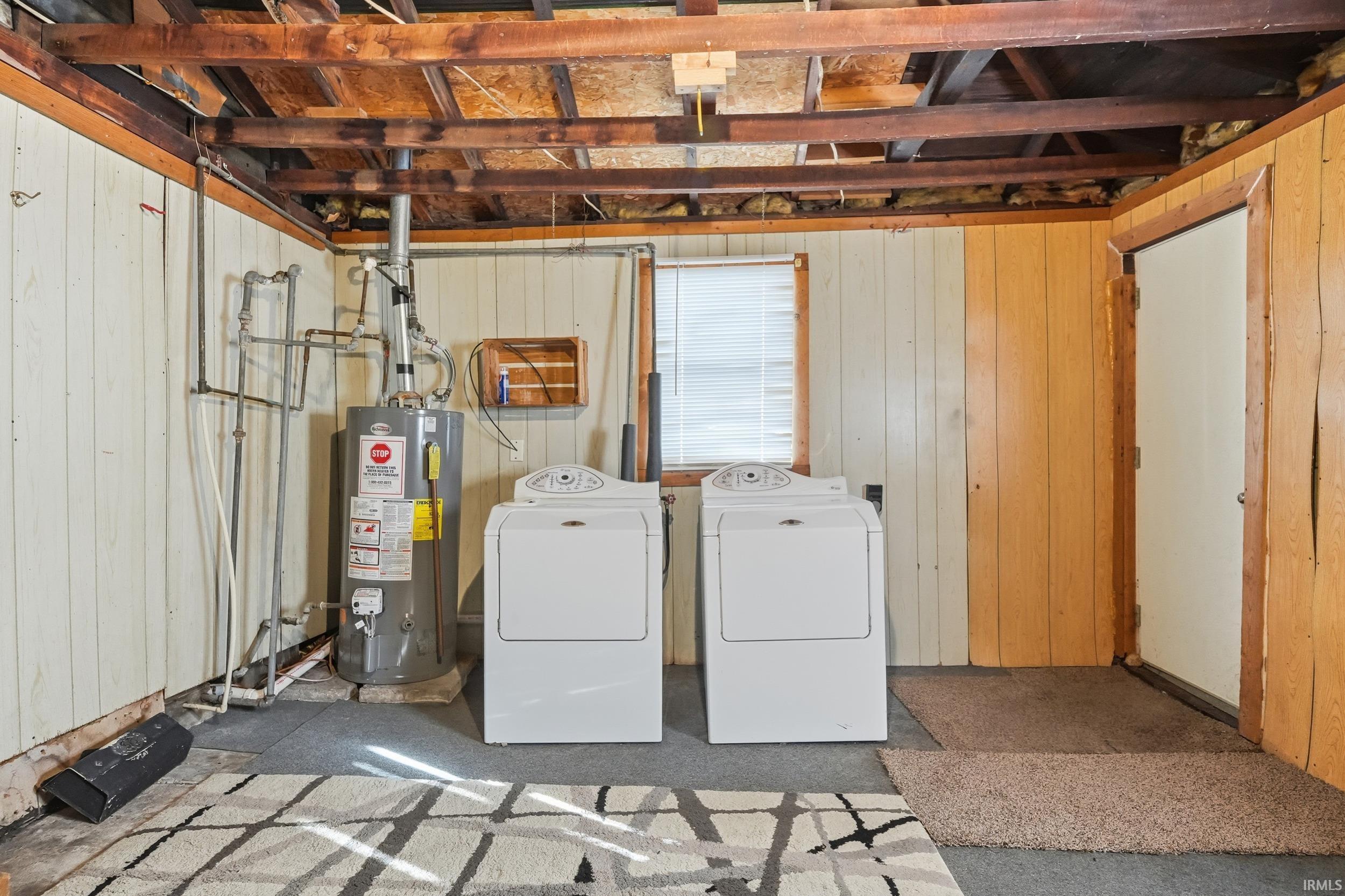 Laundry area with wood walls, water heater, and washing machine and clothes dryer