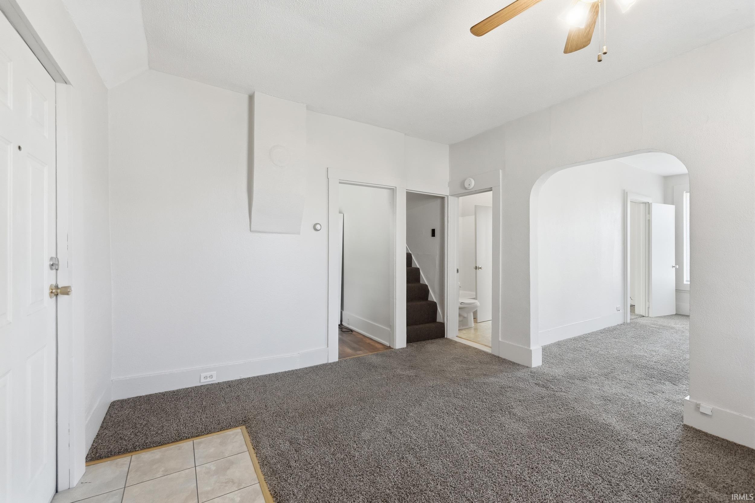 Empty room featuring light colored carpet, a ceiling fan, arched walkways, and stairs