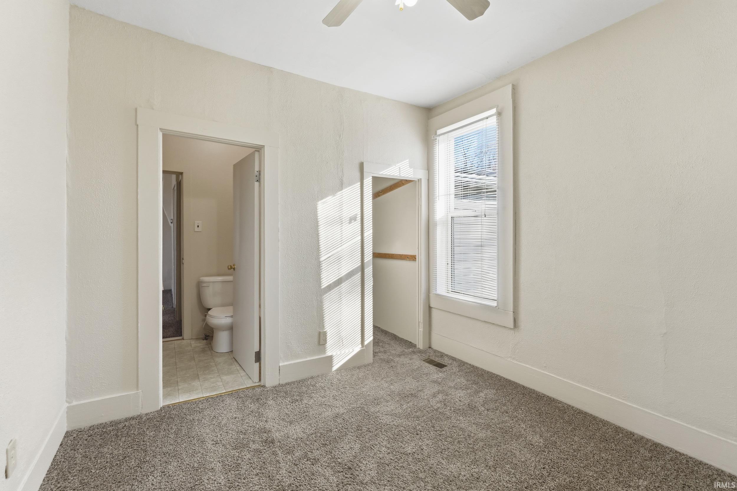 Unfurnished bedroom featuring light carpet, a ceiling fan, and ensuite bathroom