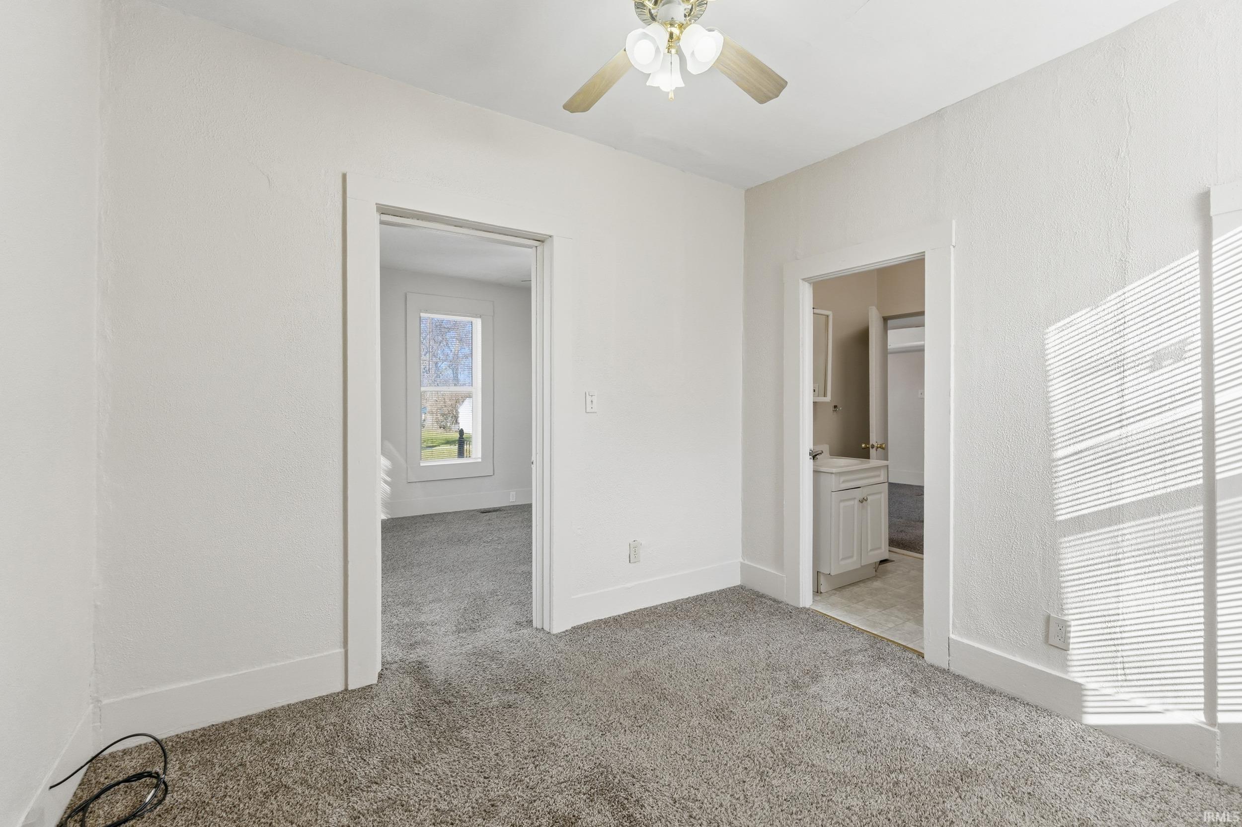 Unfurnished bedroom with light colored carpet, ensuite bathroom, and a ceiling fan