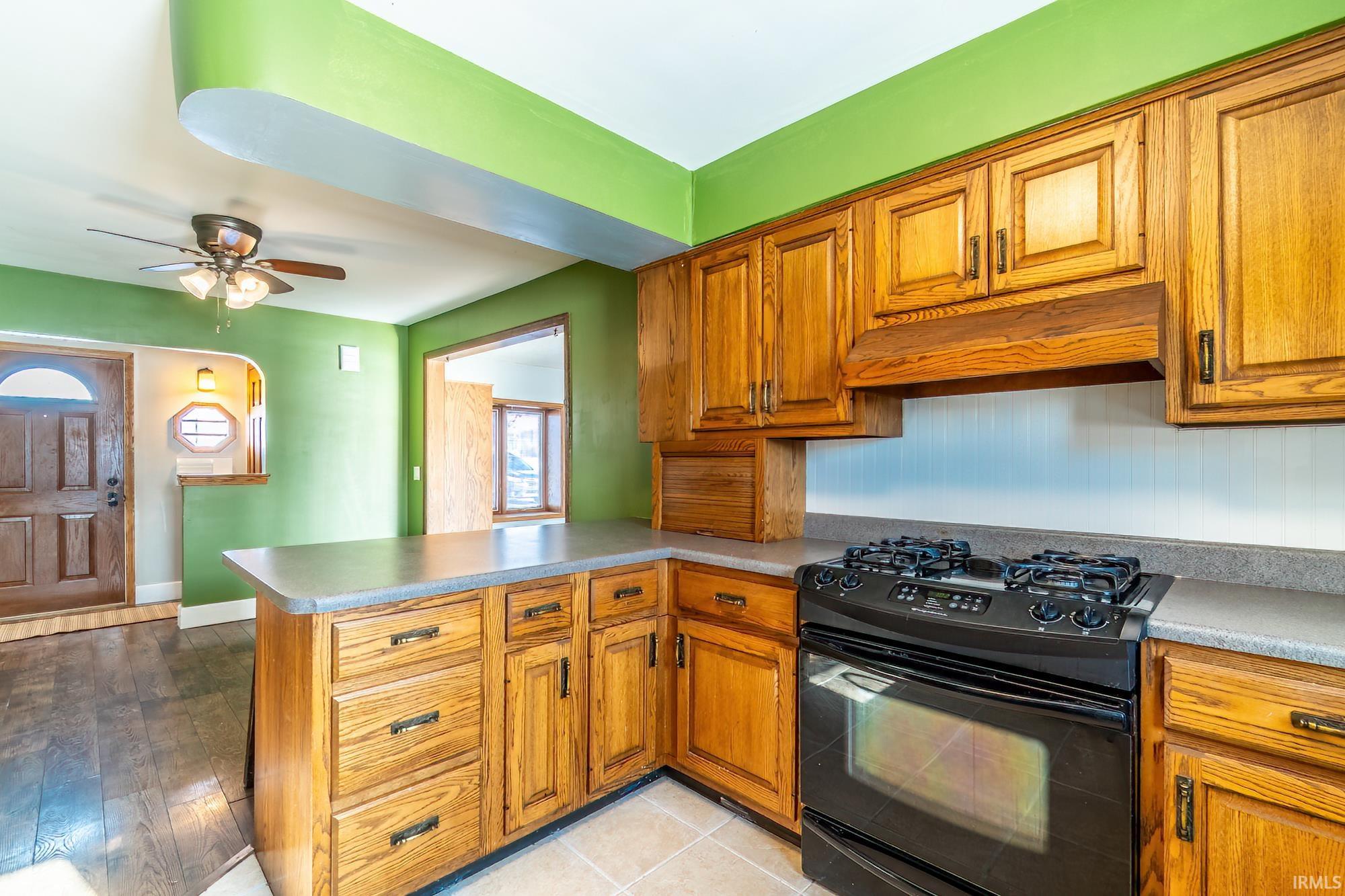 Kitchen with black gas range, brown cabinets, a peninsula, and under cabinet range hood