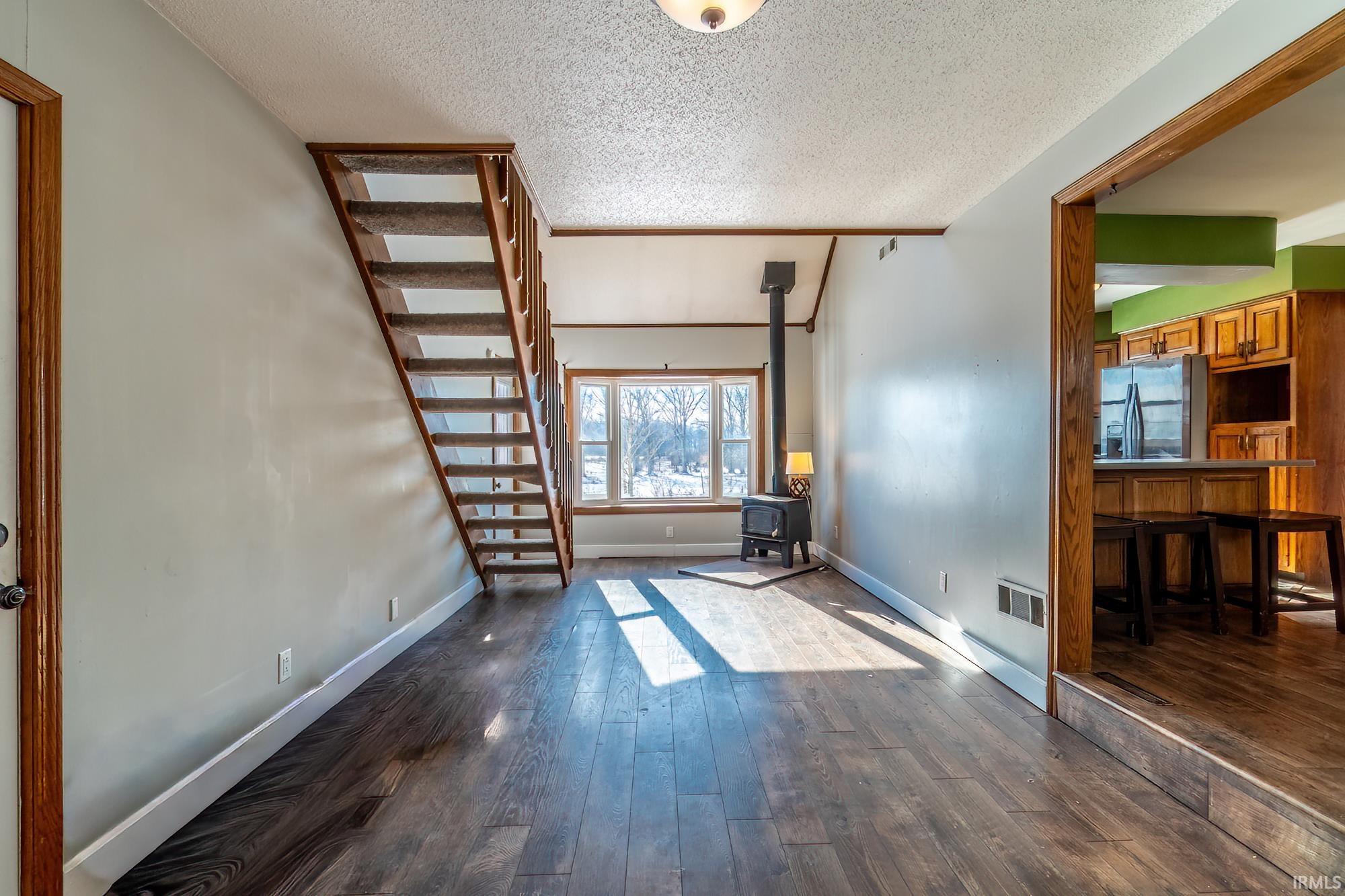 Spare room with a wood stove, dark wood-style floors, a textured ceiling, and stairway
