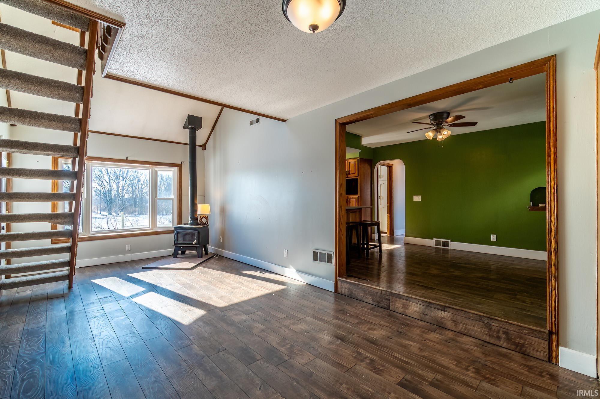Spare room with dark wood-type flooring, a wood stove, a textured ceiling, ceiling fan, and arched walkways