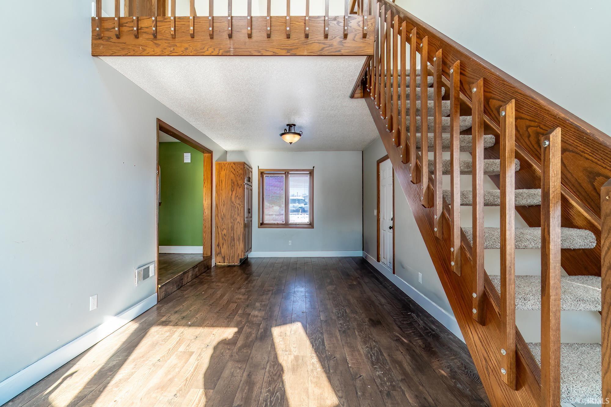 Unfurnished living room featuring stairway, dark wood finished floors, and a textured ceiling