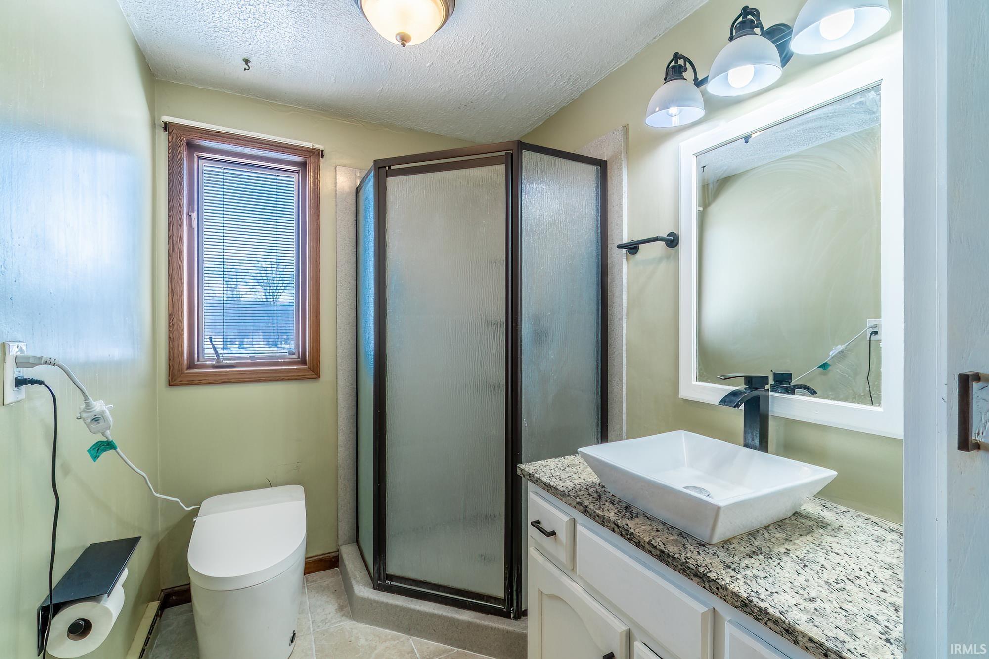 Bathroom featuring vanity, a textured ceiling, a shower stall, and light tile patterned floors