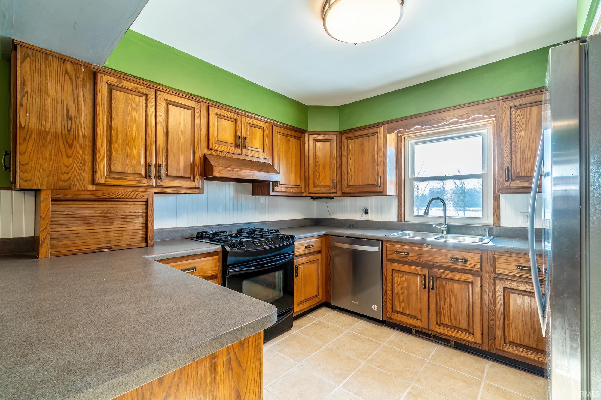 Kitchen with brown cabinets, appliances with stainless steel finishes, under cabinet range hood, and light tile patterned floors