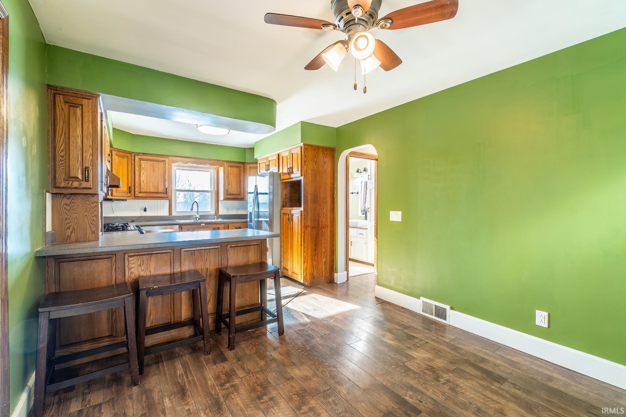 Kitchen with arched walkways, a peninsula, a breakfast bar area, dark wood-style flooring, and brown cabinetry