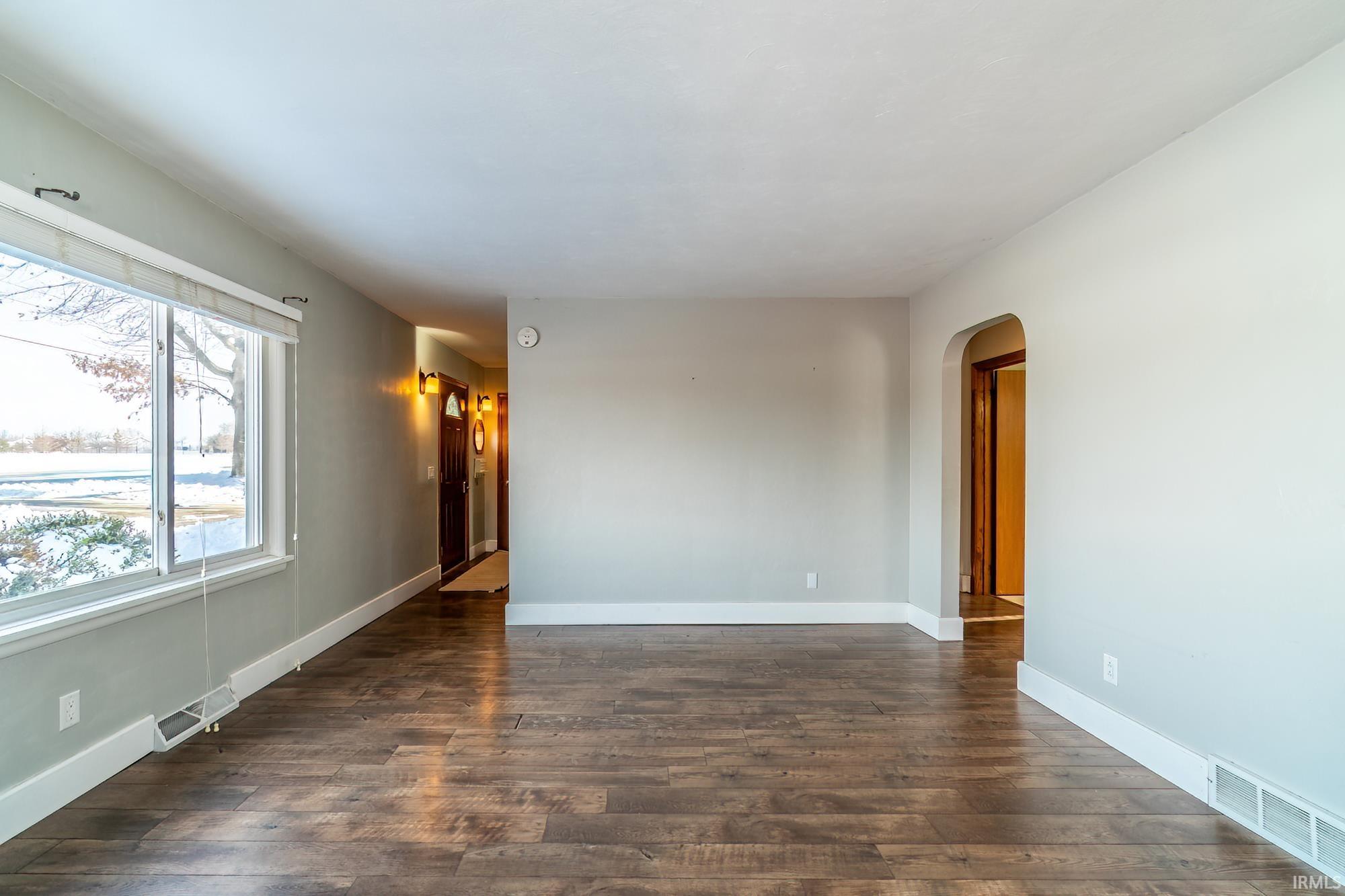 Unfurnished room featuring arched walkways and dark wood-style floors