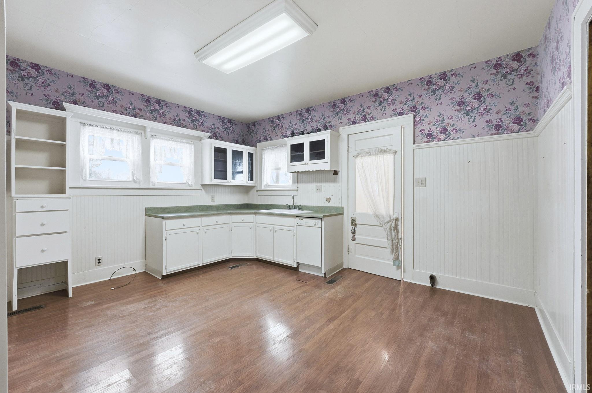 Kitchen with wallpapered walls, white cabinetry, dark wood finished floors, light countertops, and white dishwasher