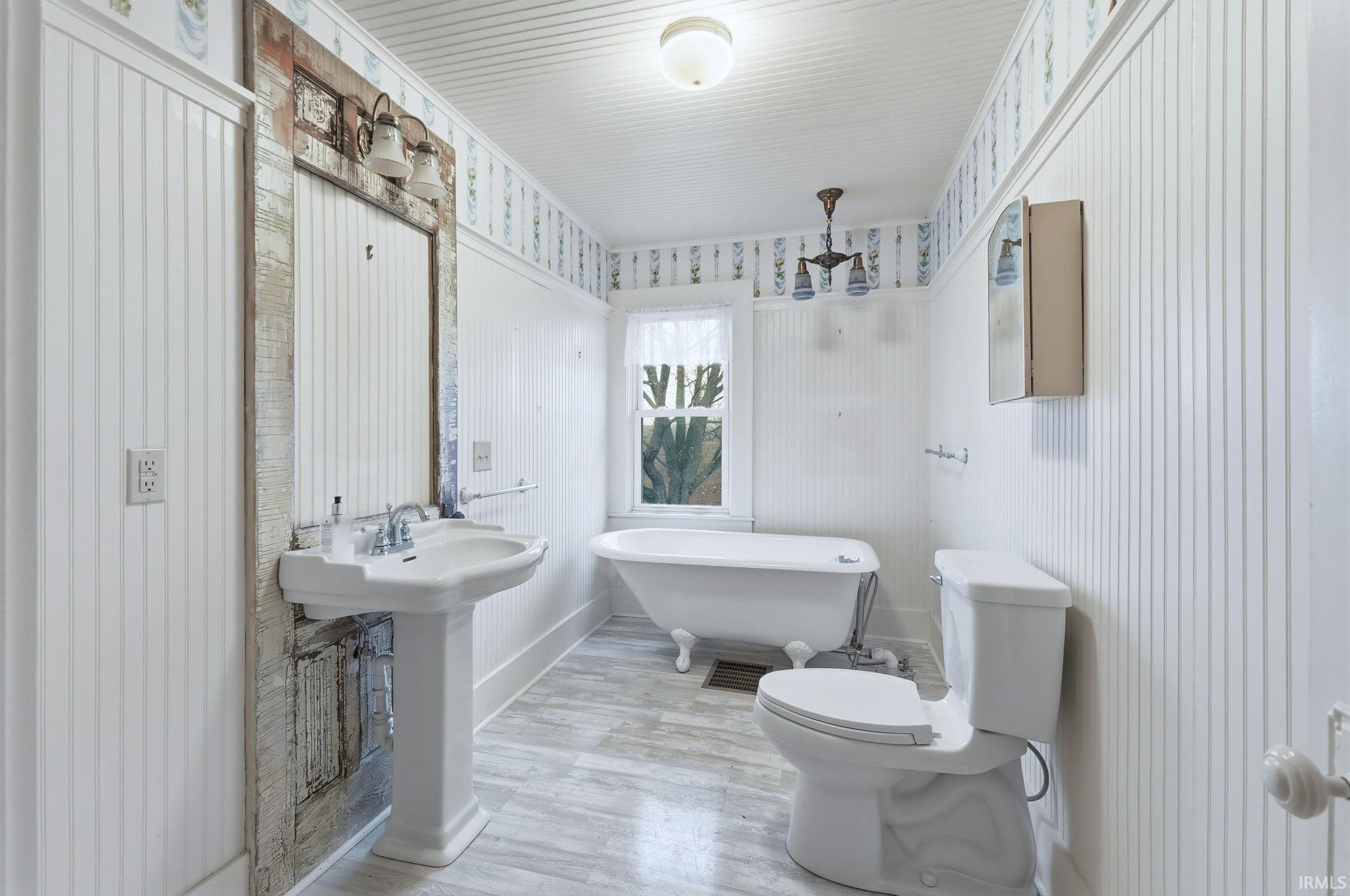 Bathroom with a soaking tub, wood finished floors, and wallpapered walls