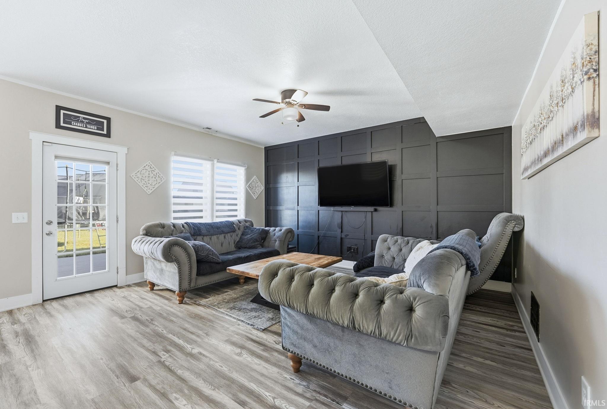 Living area with an accent wall, a ceiling fan, light wood finished floors, and a decorative wall