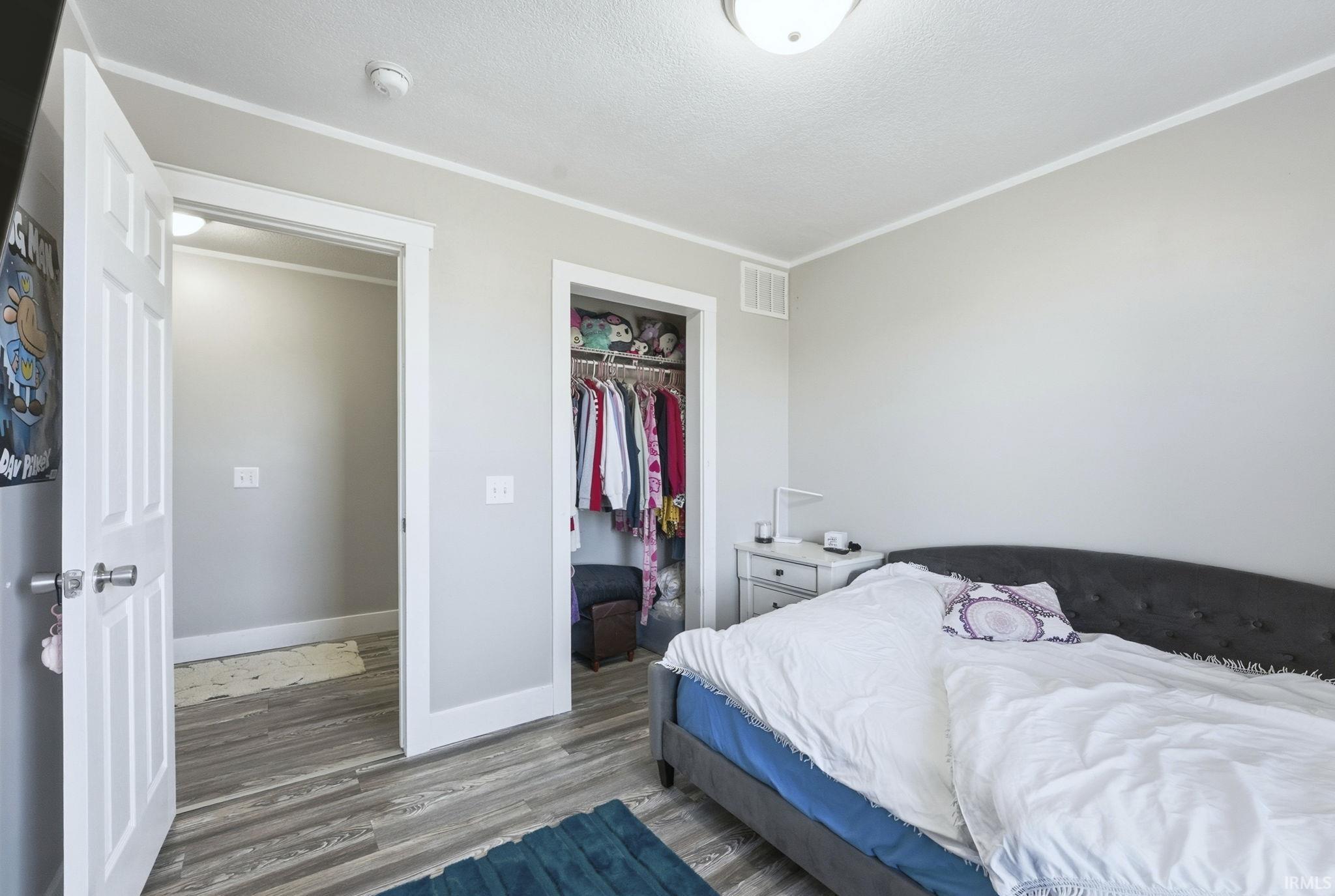 Bedroom featuring wood finished floors, ornamental molding, a closet, and a textured ceiling