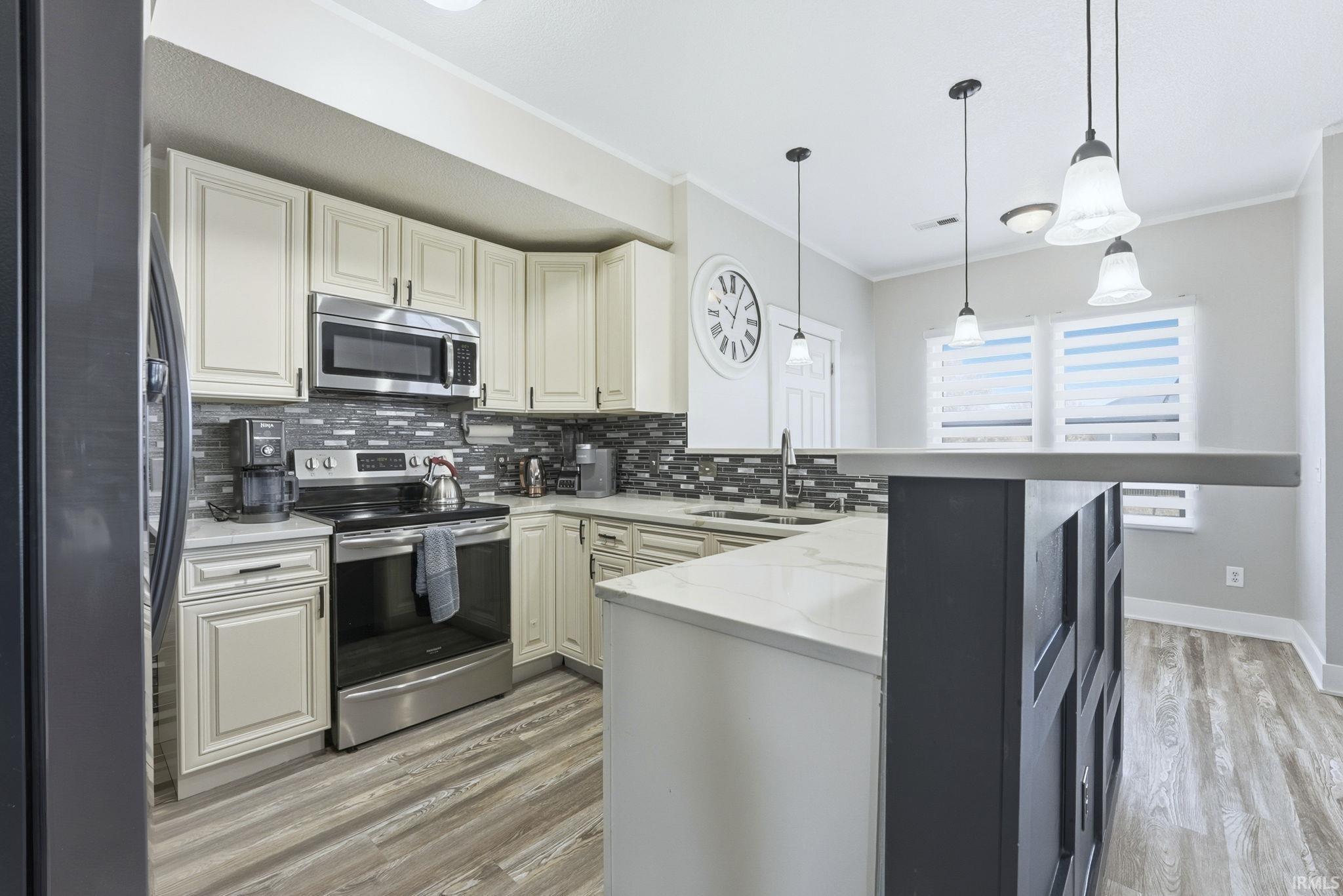 Kitchen with stainless steel appliances, pendant lighting, light stone counters, backsplash, and light wood finished floors