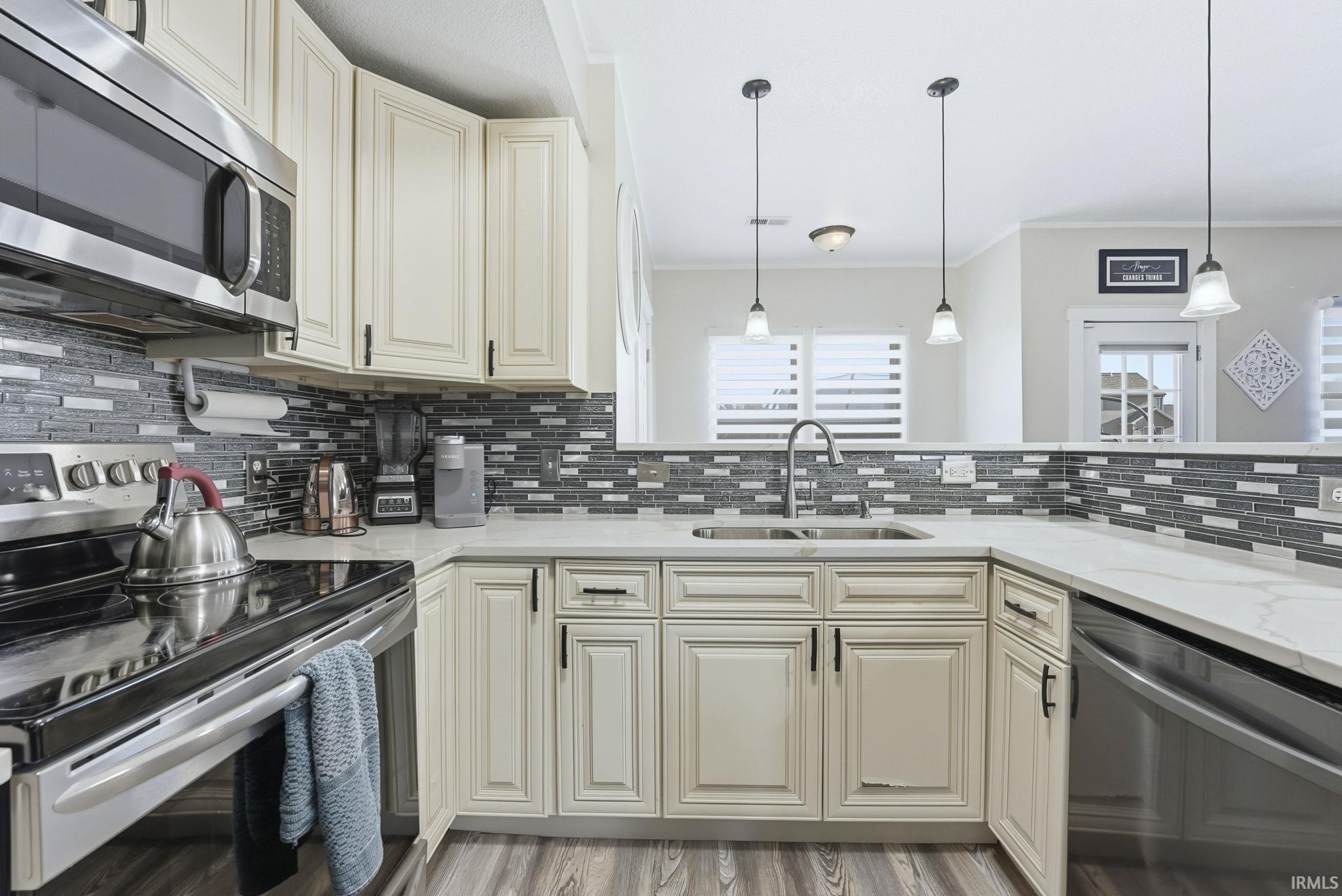 Kitchen featuring stainless steel appliances, cream cabinetry, decorative backsplash, and crown molding