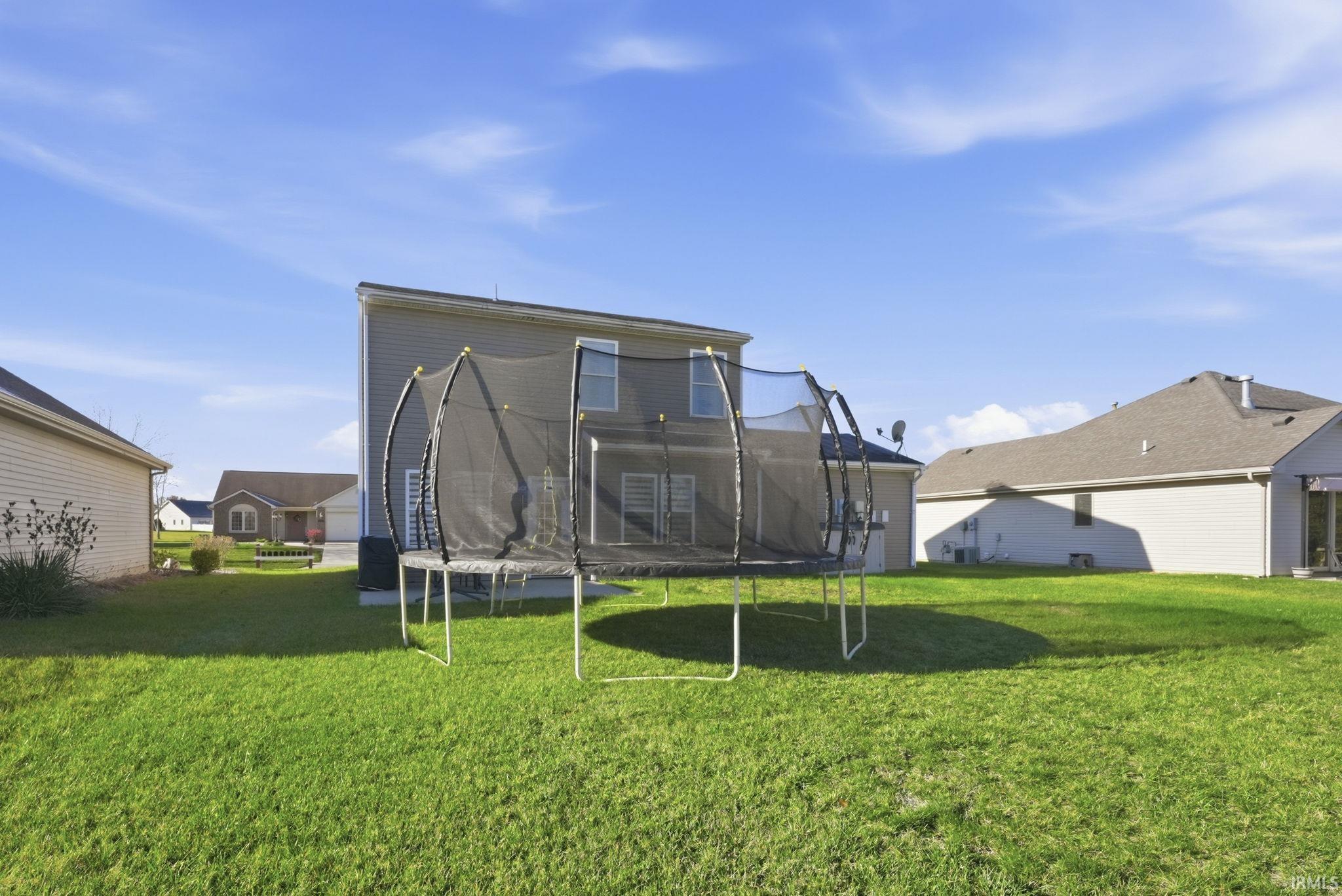 Back of property featuring a trampoline and a yard