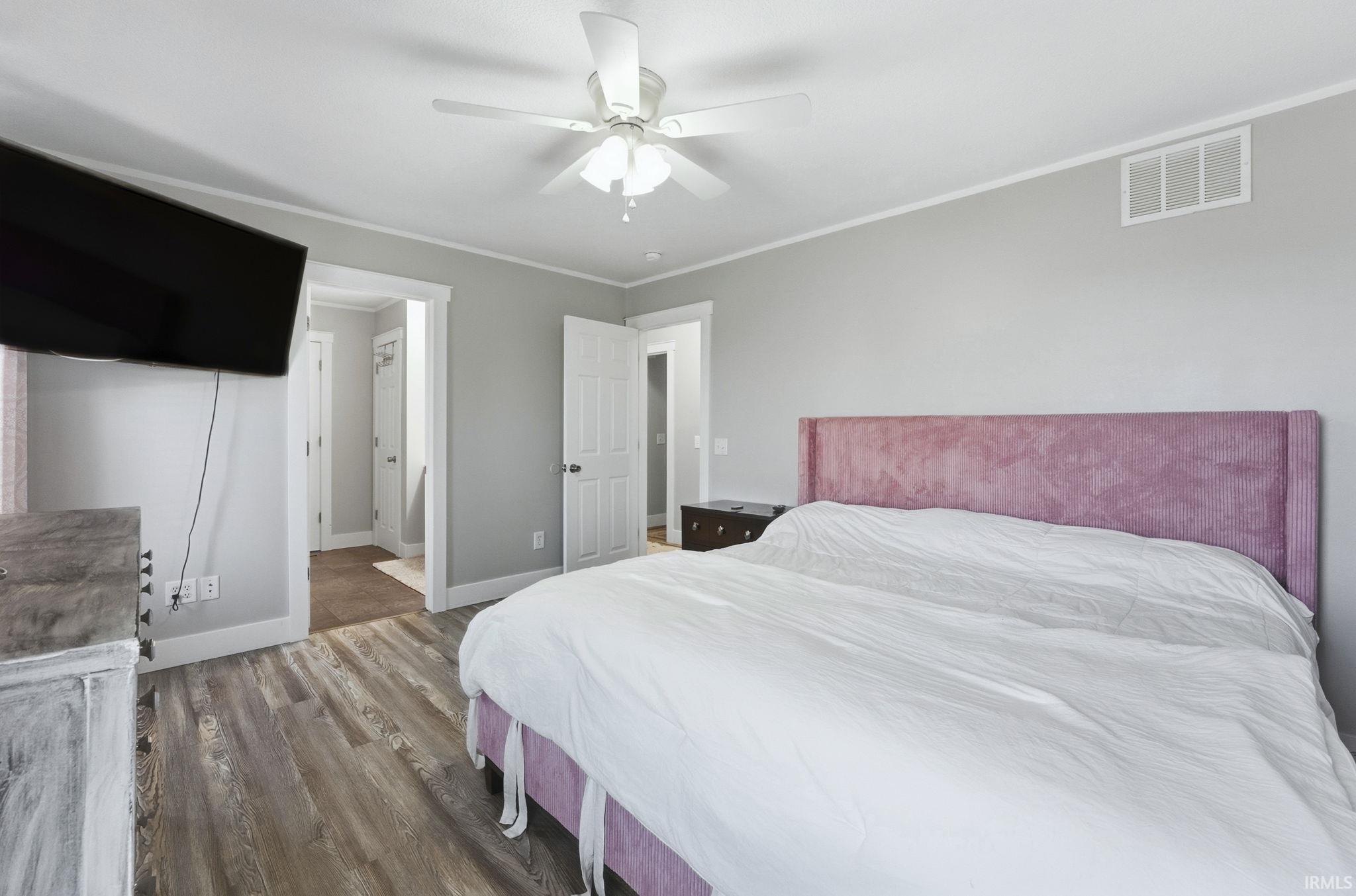 Bedroom with wood finished floors, ensuite bathroom, crown molding, and a ceiling fan