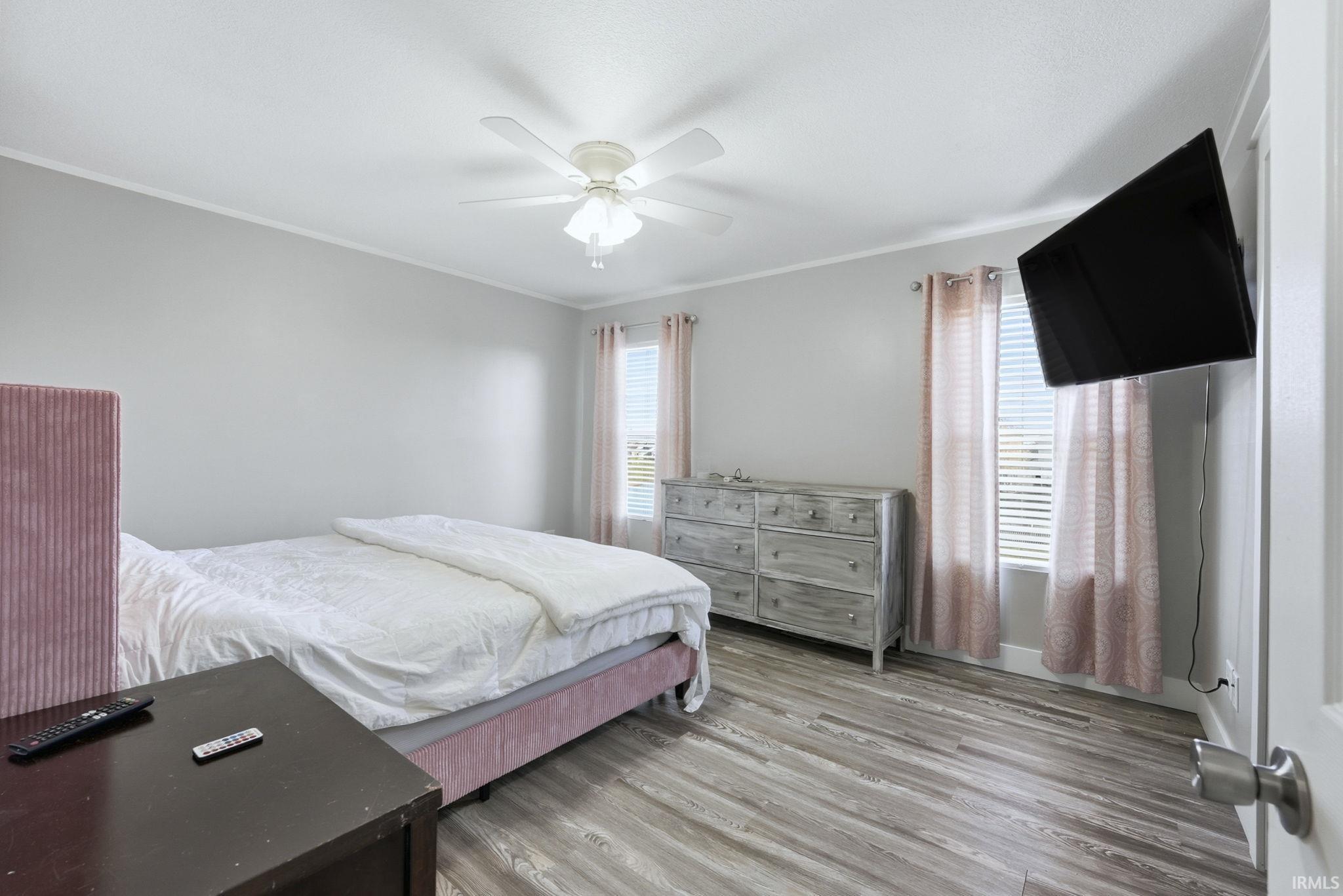 Bedroom with crown molding, light wood-style flooring, multiple windows, and a ceiling fan