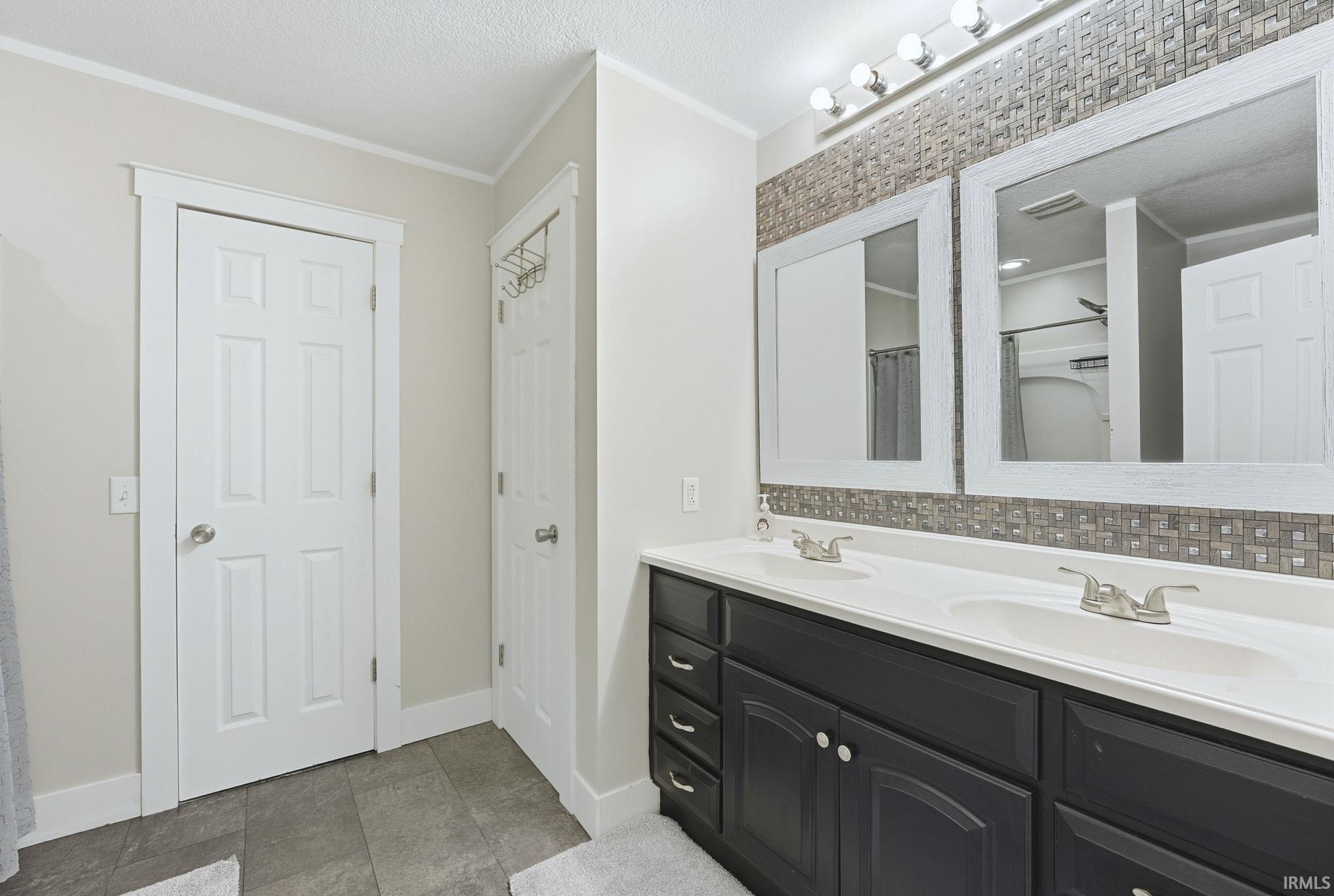 Bathroom featuring double vanity, crown molding, a textured ceiling, curtained shower, and dark tile patterned flooring