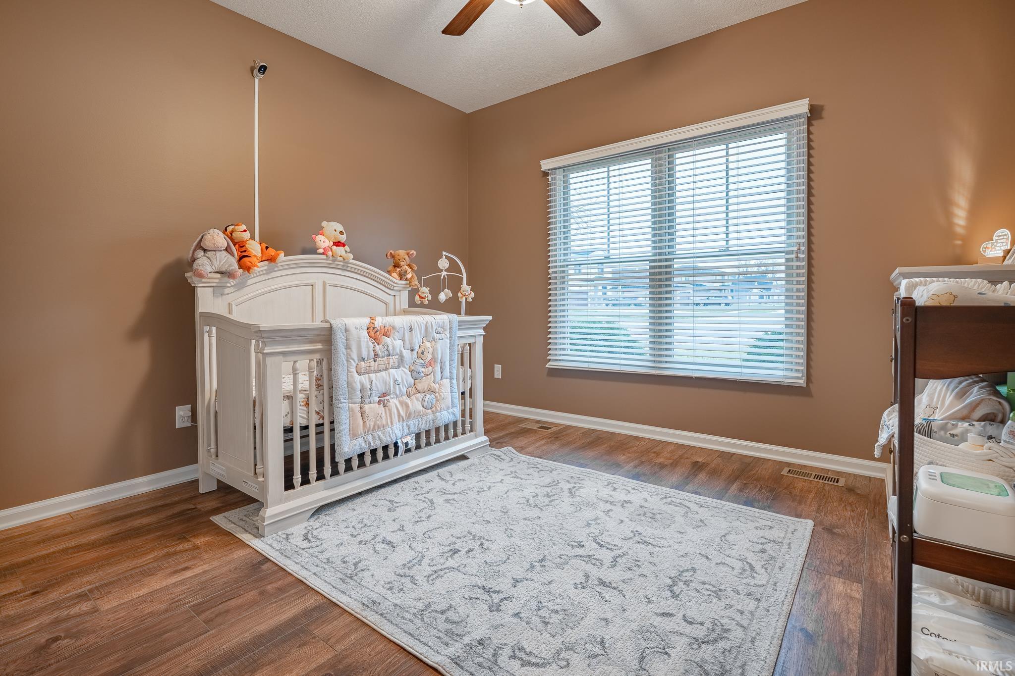 Bedroom featuring dark wood-type flooring, a ceiling fan, and a nursery area